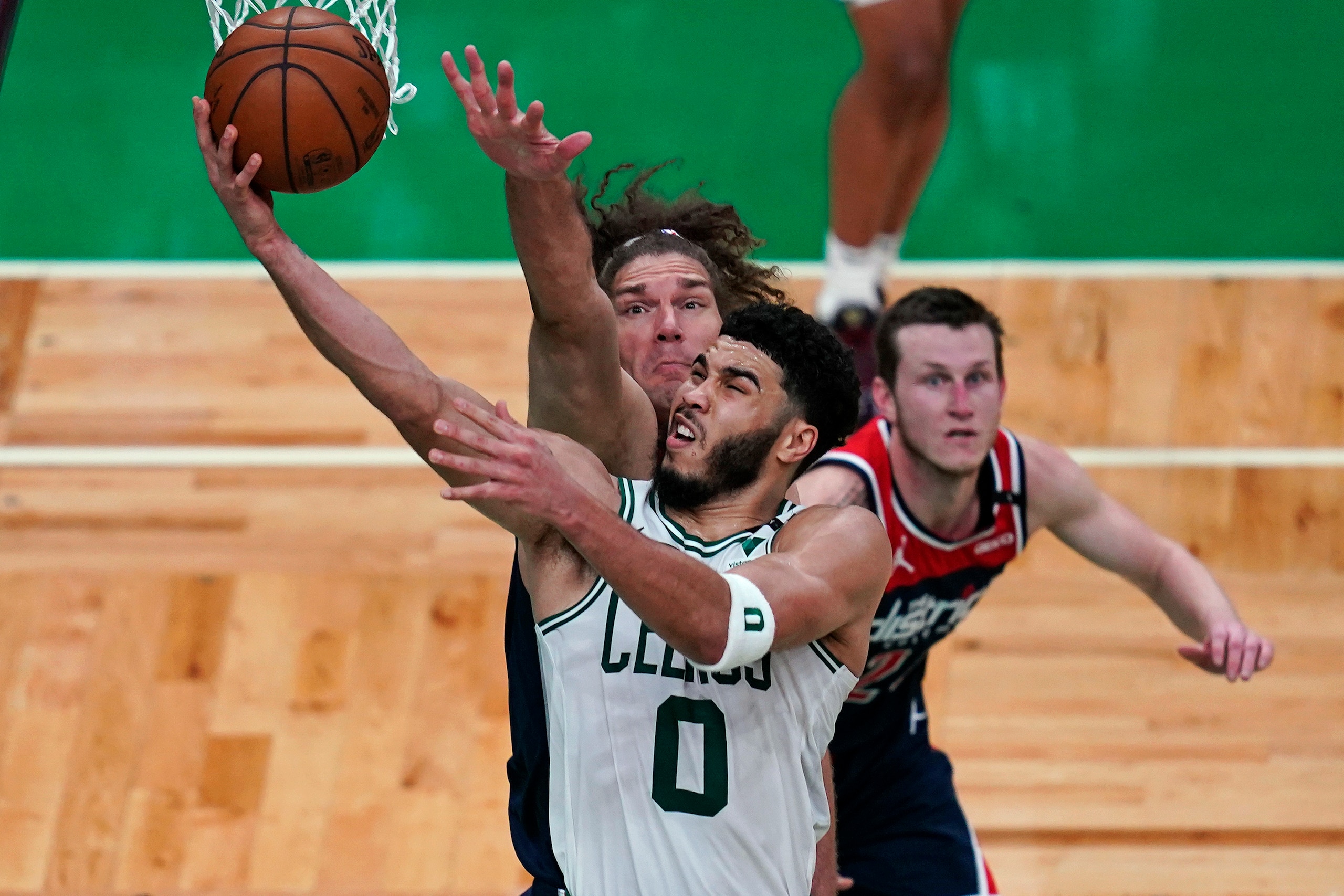 Boston Celtics forward Jayson Tatum (0) drives to the basket past Washington Wizards center Robin Lopez, rear left, during the second half of an NBA basketball Eastern Conference play-in game Tuesday, May 18, 2021, in Boston. At rear right is Wizards guard Garrison Mathews. (AP Photo/Charles Krupa)