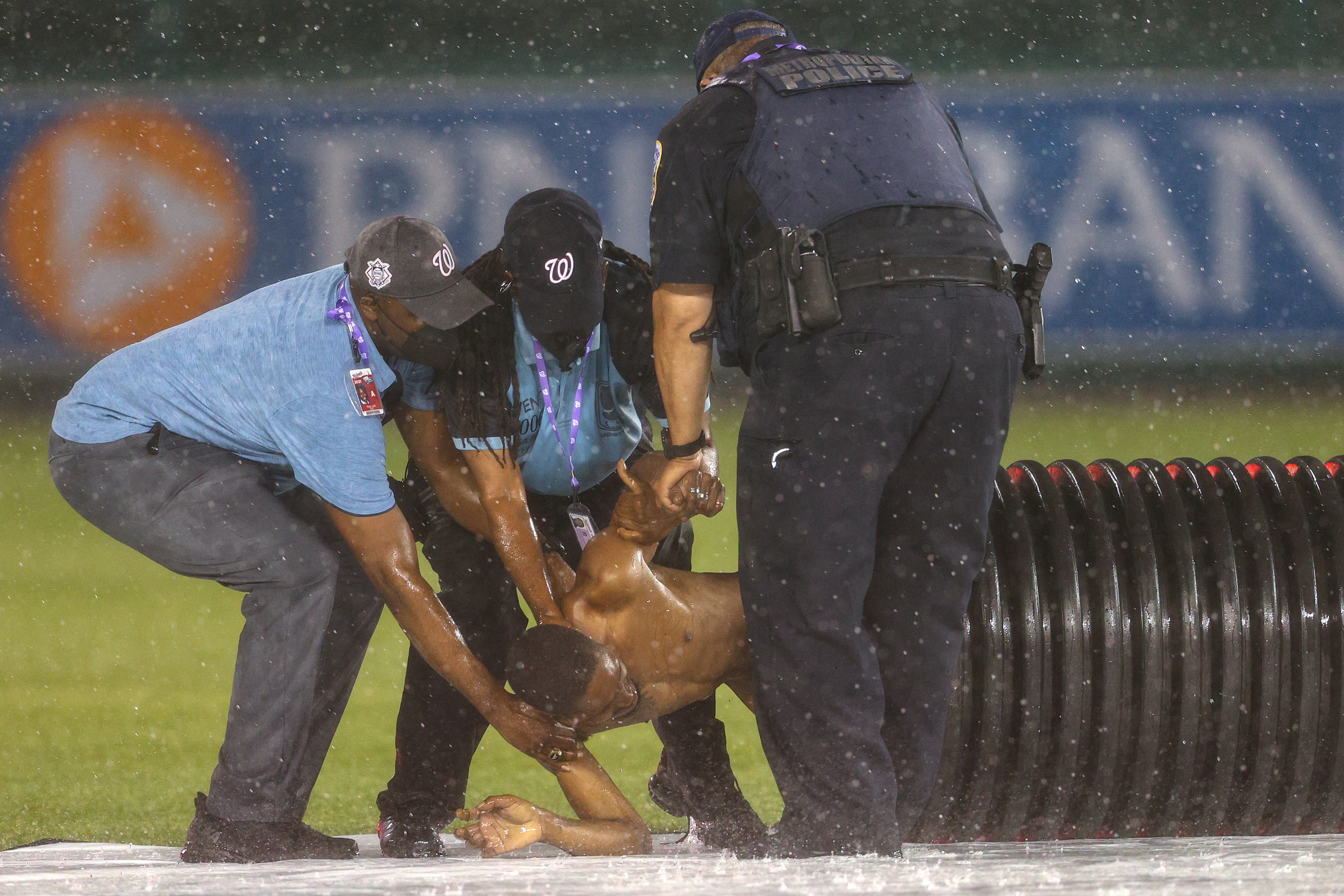 WASHINGTON, DC - MAY 26: A streaker is pulled from the infield tarp roller by law enforcement and security during a rain delay between the Cincinnati Reds and against the Washington Nationals at Nationals Park on May 26, 2021 in Washington, DC. (Photo by Patrick Smith/Getty Images)