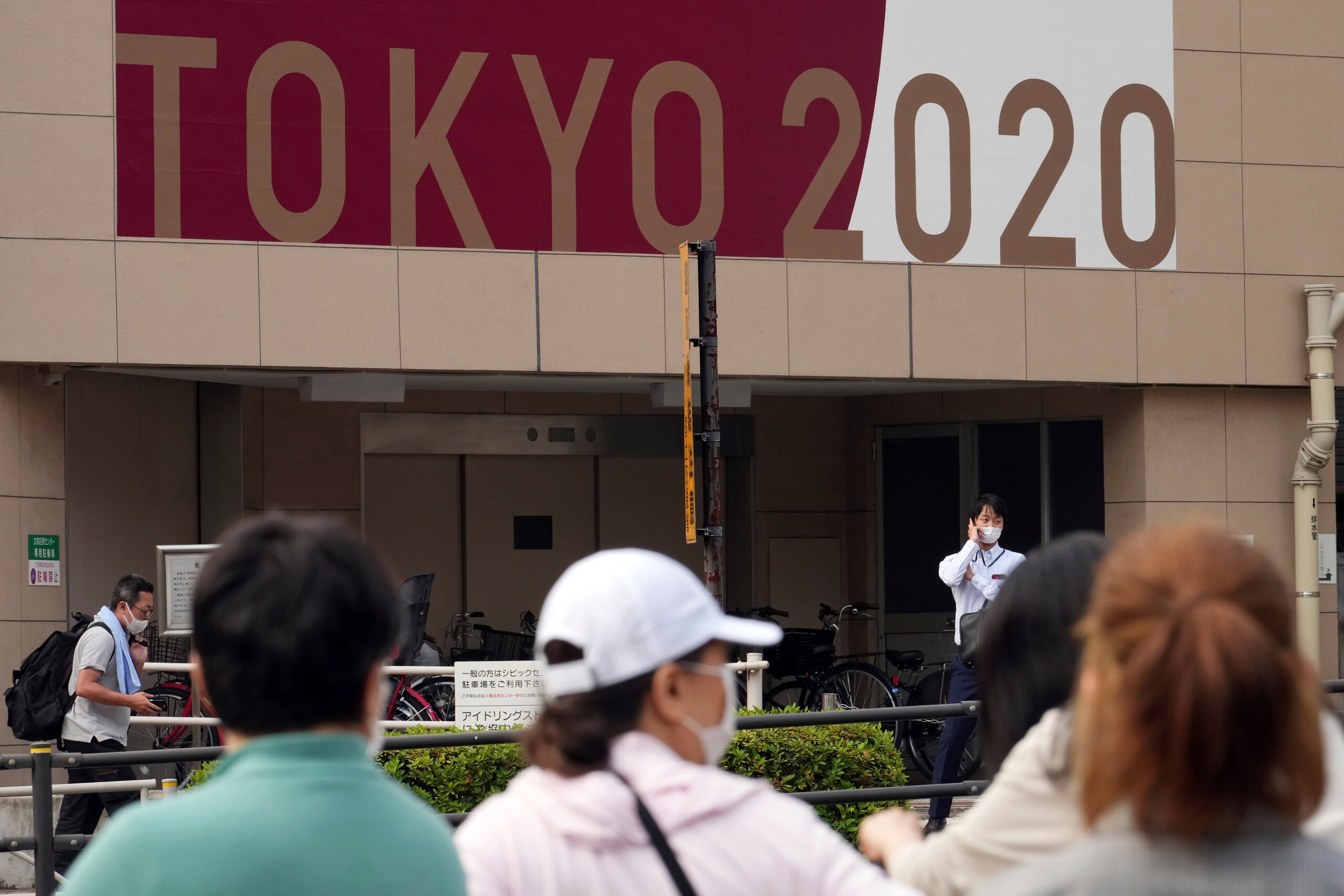 People wearing masks to help protect against the spread of the coronavirus wait for traffic light to change near a banner to promote the Tokyo Olympic Games Tuesday, May 25, 2021, in Tokyo. (AP Photo/Eugene Hoshiko)