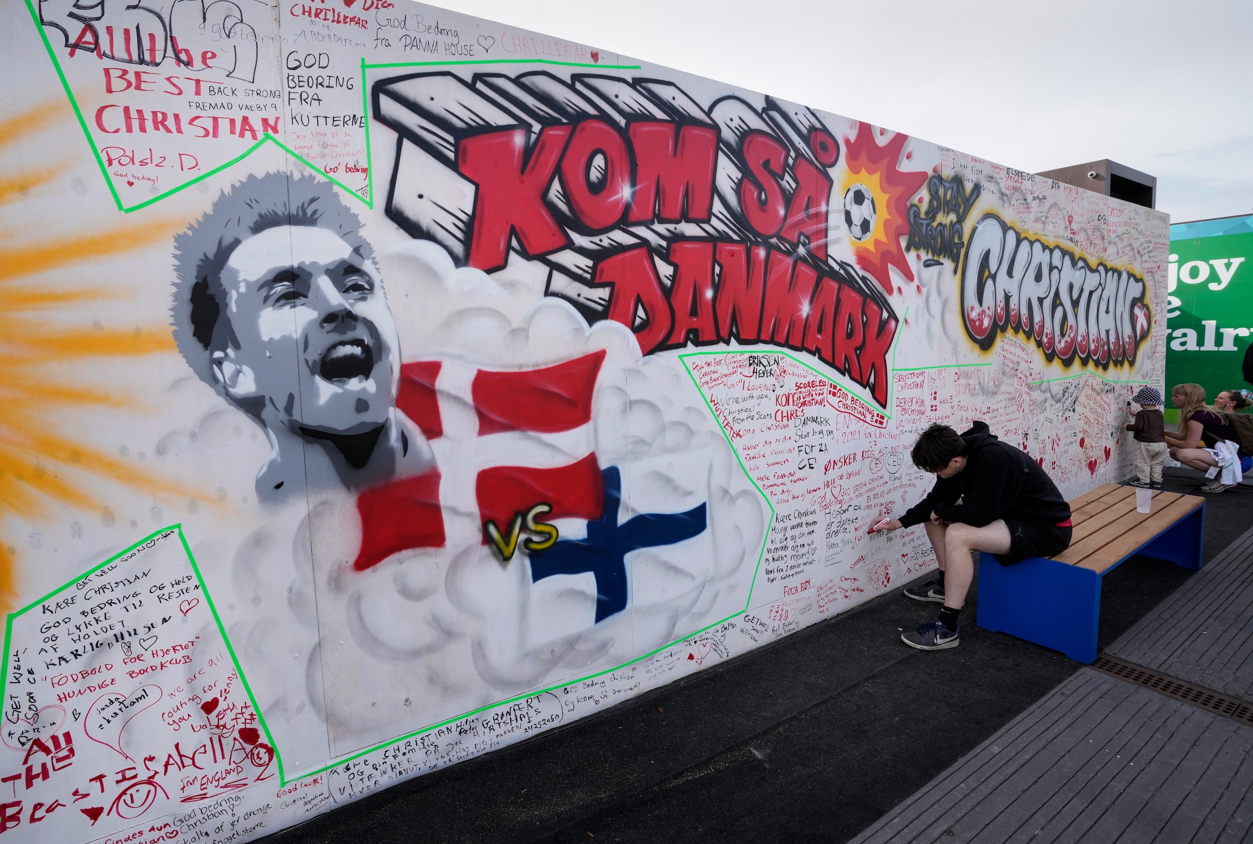 People writing well wishes at a graffiti for Danish player Christian Eriksen on a wall at the fanzone in Copenhagen, Denmark, Monday, June 14, 2021. Eriksen remains in hospital after he collapsed on the pitch during the European Championship game against Finland on Saturday and needed CPR from medical staff before regaining consciousness. (AP Photo/Martin Meissner)