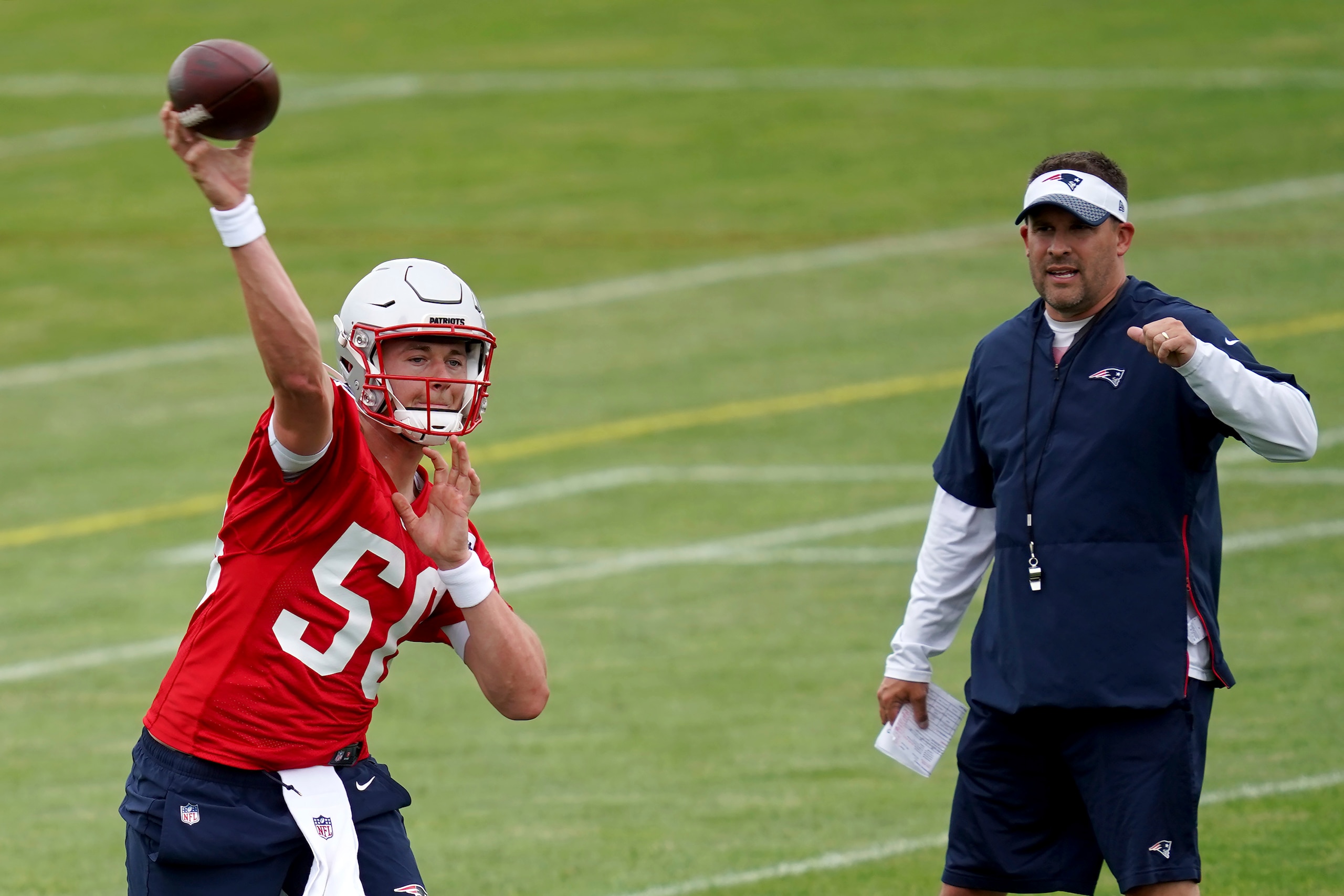 New England Patriots quarterback Mac Jones throws a pass as offensive coordinator Josh McDaniels looks on during NFL football practice in Foxborough, Mass., Friday, June 4, 2021. (AP Photo/Mary Schwalm)