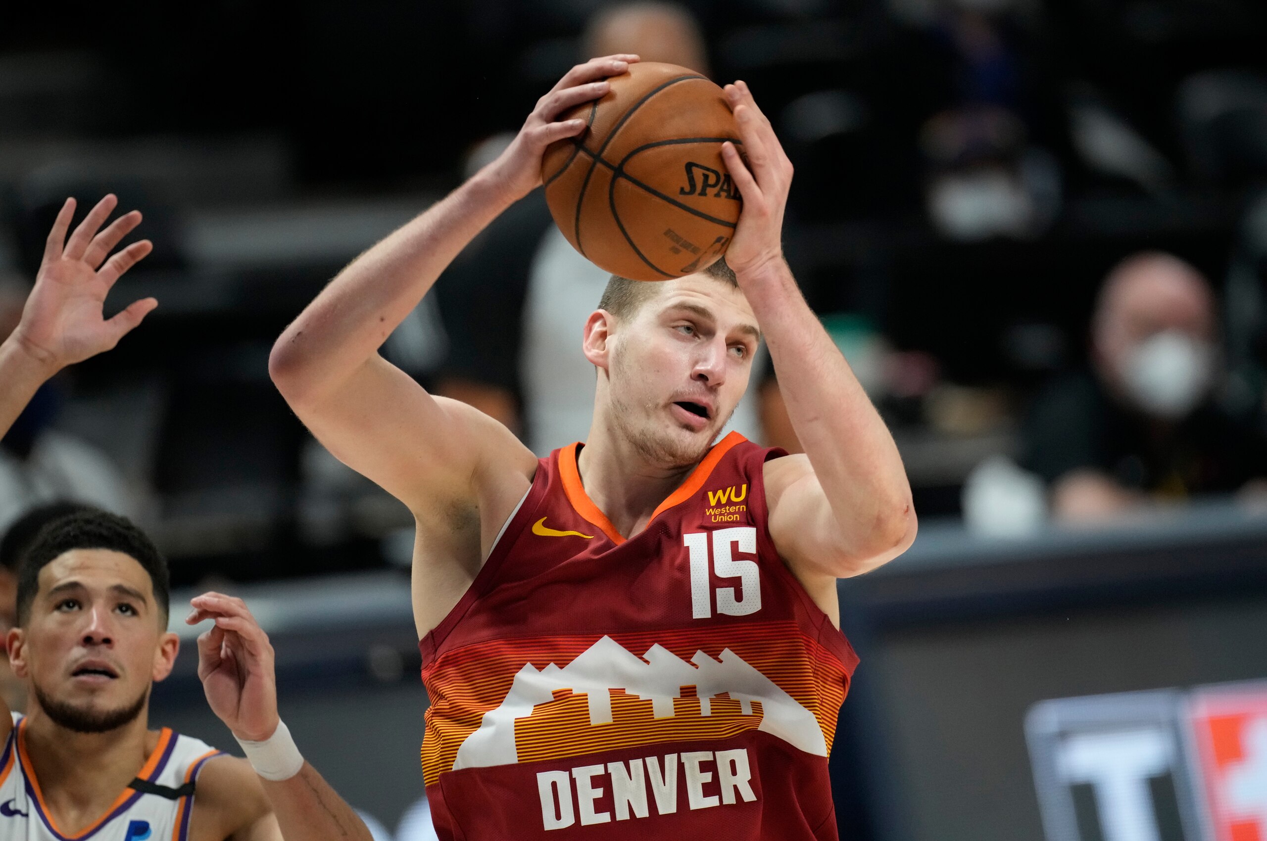 Denver Nuggets center Nikola Jokic, right, pulls in a rebound in front of Phoenix Suns guard Devin Booker in the first half of Game 4 of an NBA second-round playoff series Sunday, June 13, 2021, in Denver. (AP Photo/David Zalubowski)