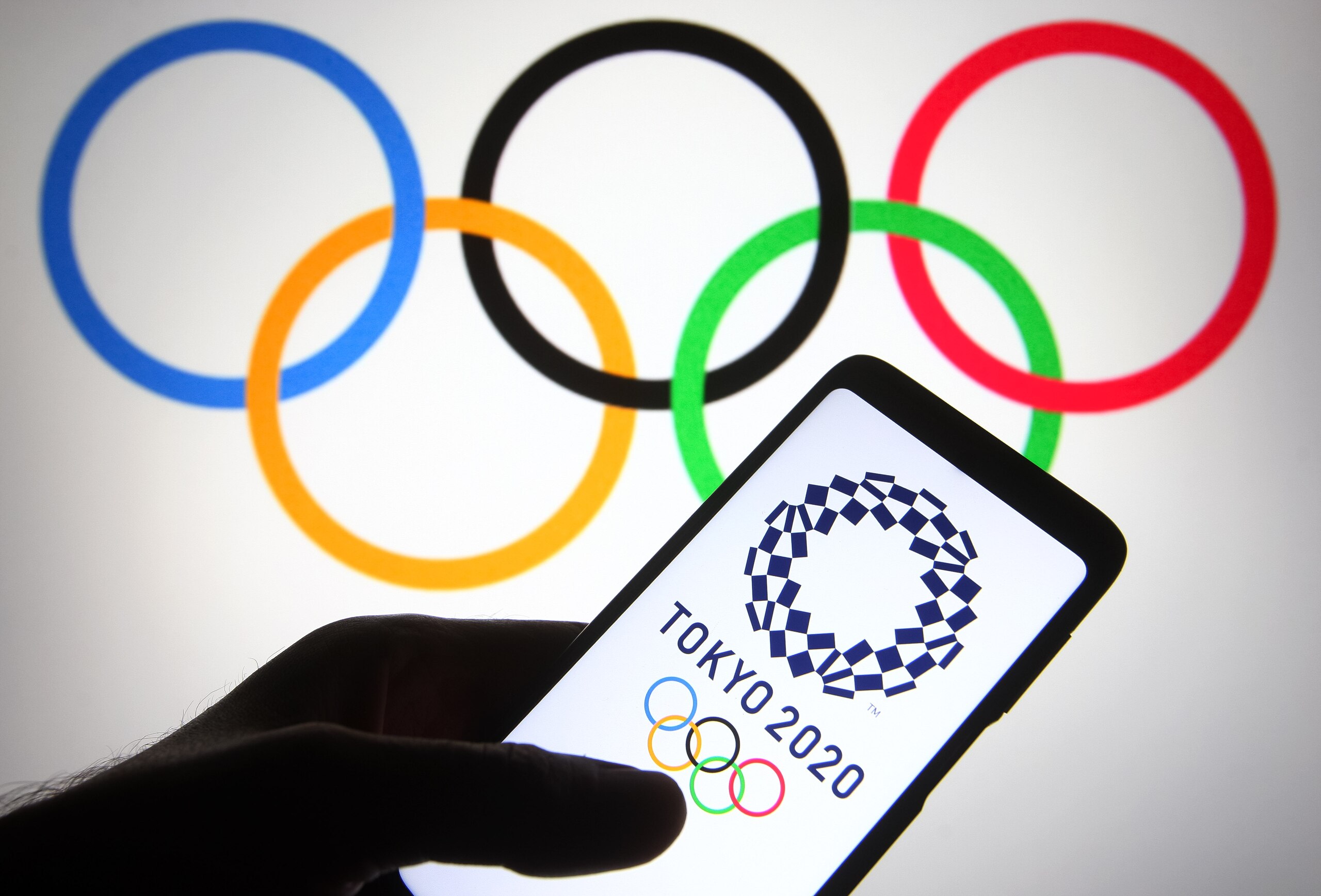 UKRAINE - 2021/06/18: In this photo illustration, Tokyo 2020 Olympic Games (2020 Summer Olympics) logo is seen on a smartphone in front of the Olympic Rings. 
The 2020 Summer Olympic Games are scheduled to take place in the Japanese capital Tokyo from 23 July till 8 August, reportedly by media.
in the background. (Photo Illustration by Pavlo Gonchar/SOPA Images/LightRocket via Getty Images)