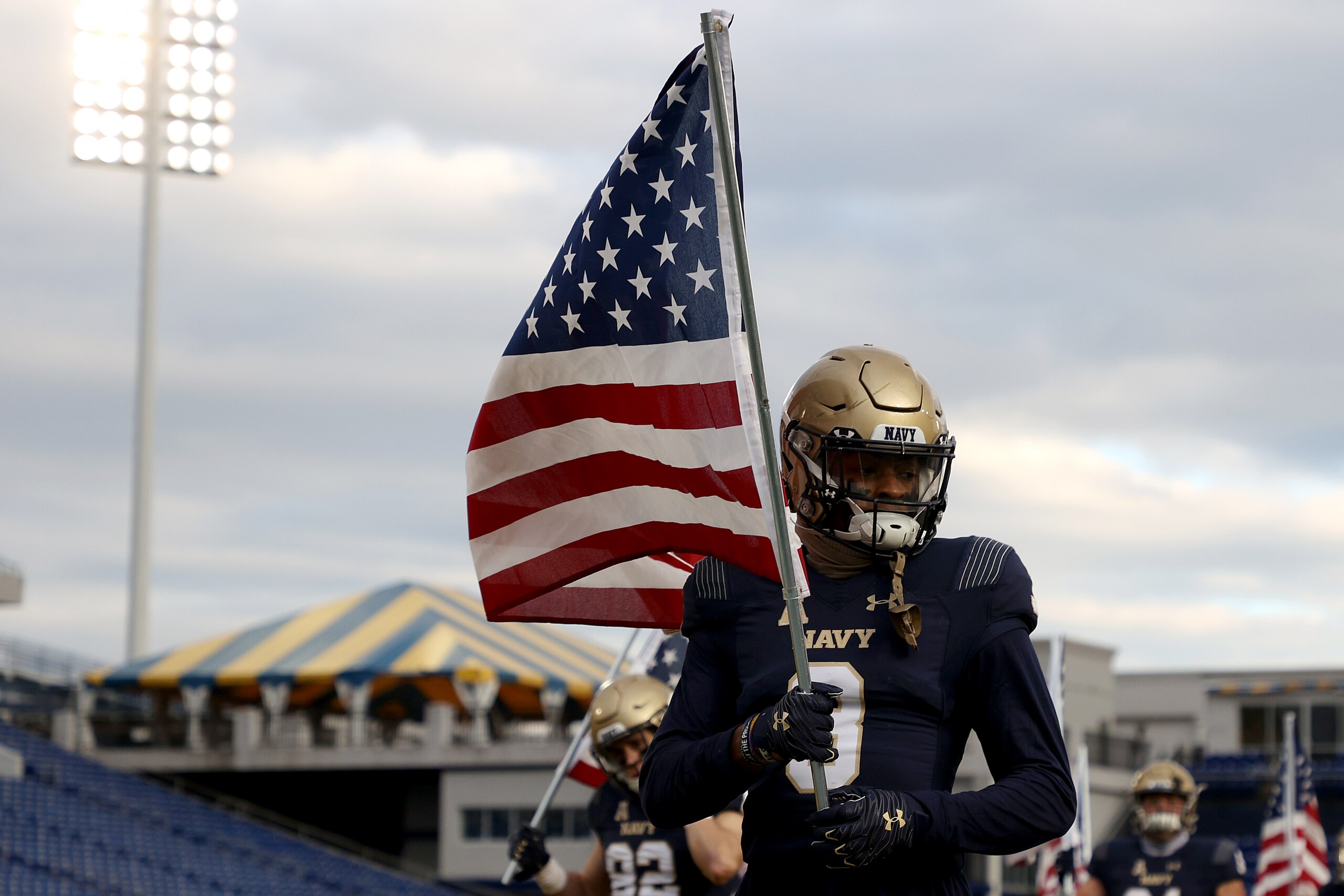 ANNAPOLIS, MARYLAND - DECEMBER 05: Cameron Kinley #3 of the Navy Midshipmen carries an American flag as the team takes the field against the Tulsa Golden Hurricane at Navy-Marine Corps Memorial Stadium on December 05, 2020 in Annapolis, Maryland. (Photo by Rob Carr/Getty Images)