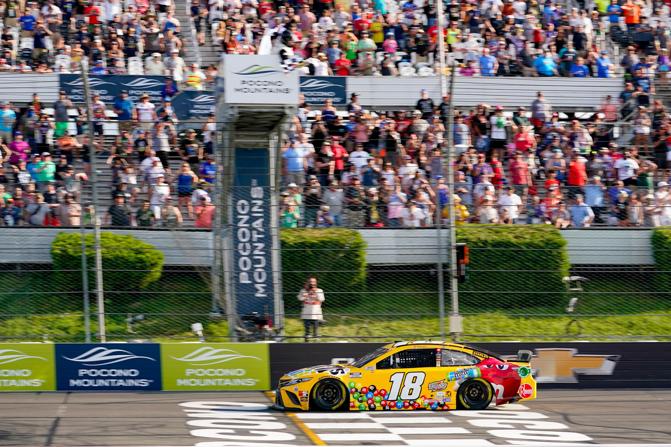 Kyle Busch (18) takes the checker flag to win the NASCAR Cup Series auto race at Pocono Raceway, Sunday, June 27, 2021, in Long Pond, Pa. (AP Photo/Matt Slocum)