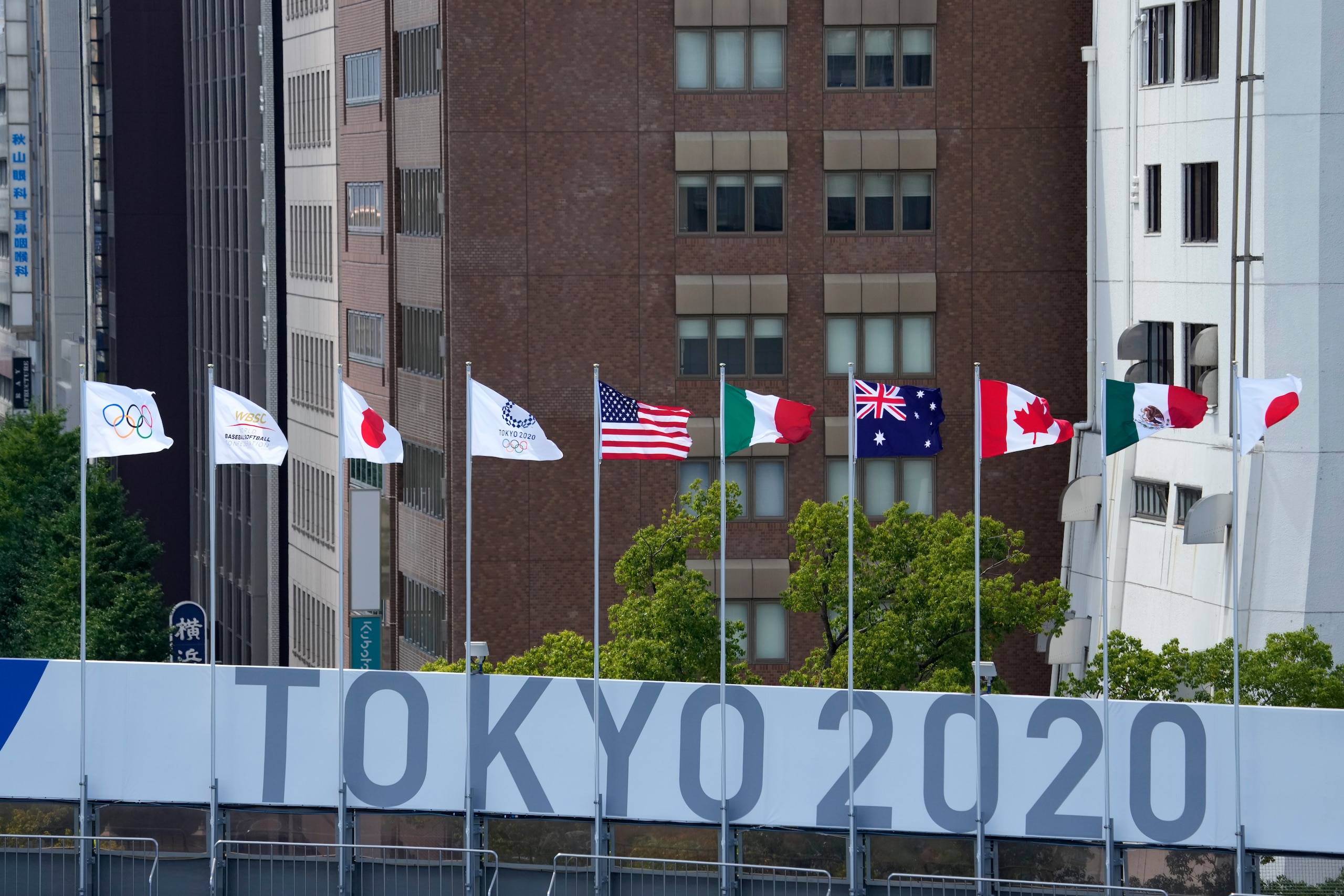 Buildings rise beyond signage for the 2020 Summer Olympics at Yokohama Baseball Stadium during softball practice Saturday, July 17, 2021, in Yokohama, Japan. (AP Photo/Charlie Riedel)