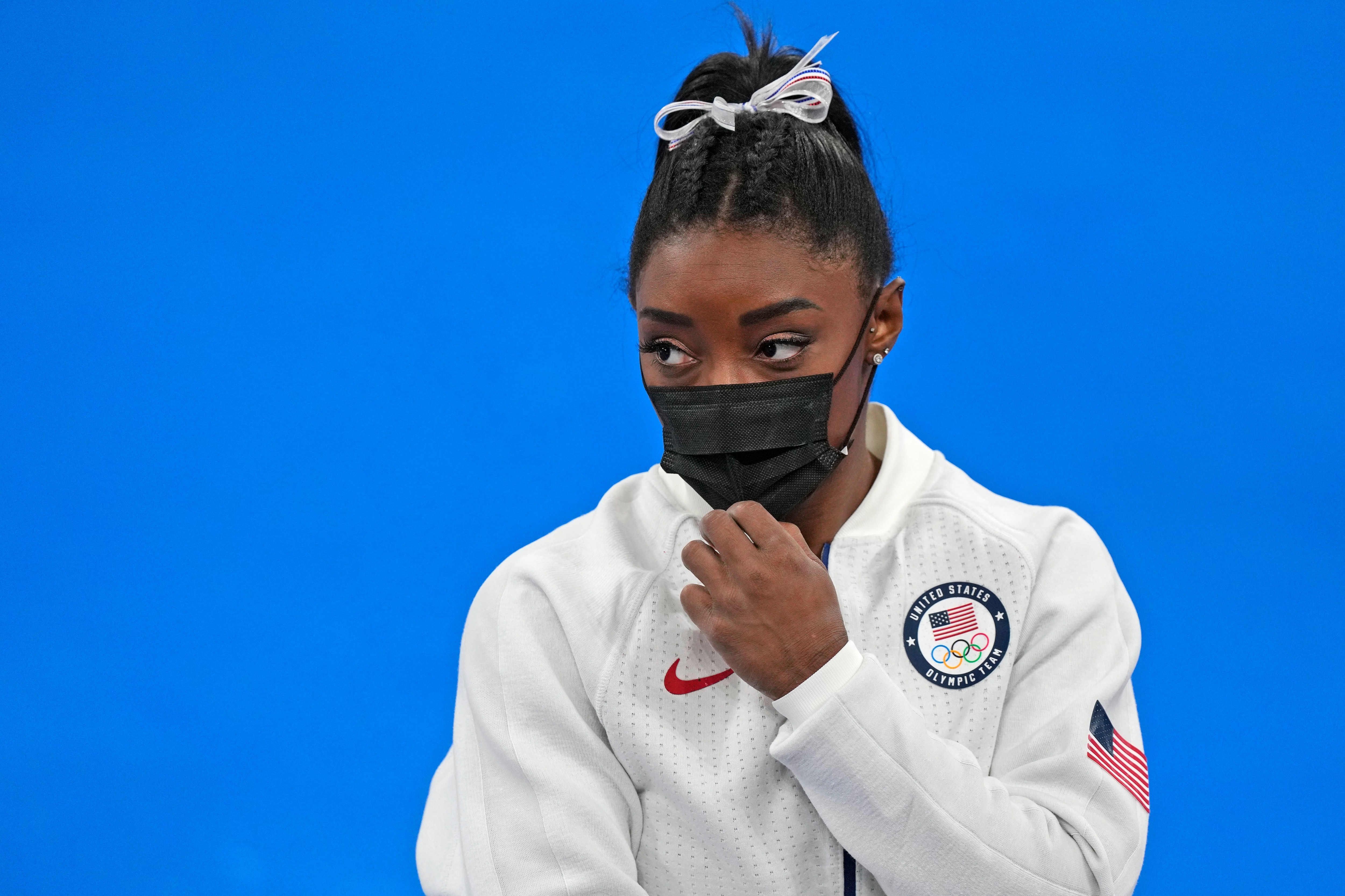 Simone Biles, of the United States, stands wearing a mask after she exited the team final with apparent injury, at the 2020 Summer Olympics, Tuesday, July 27, 2021, in Tokyo. The 24-year-old reigning Olympic gymnastics champion Biles huddled with a trainer after landing her vault. She then exited the competition floor with the team doctor. (AP Photo/Natacha Pisarenko)
