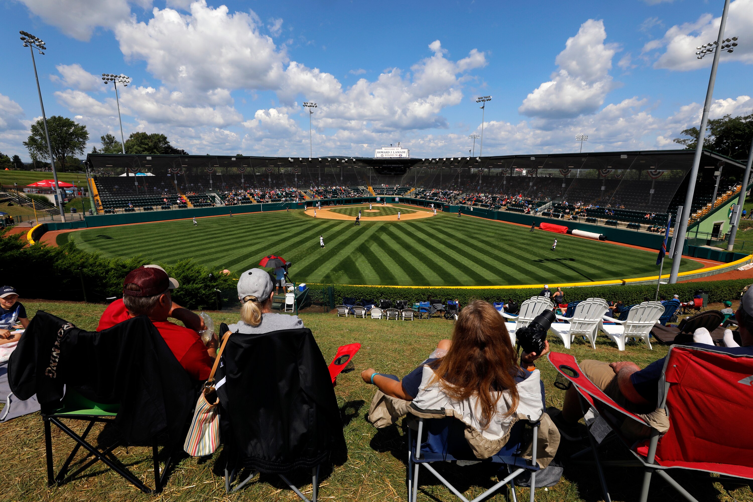 In this Aug. 23, 2018, photo, Little League fans watch a consolation baseball game between Coeur D'Alene, Idaho and Barcelona, Spain at the Little League World Series tournament in South Williamsport, Pa. Little League has been benched. The youth baseball program that boasts more than 2.5 million kids spread over 6,500 programs in 84 countries is on hold at least until May 11 due to the corona virus pandemic.  Even that target date for a return to the sports lineup seems optimistic, and the fate of its signature event, the Little League World Series in August in South Williamsport, Pennsylvania is unclear. (AP Photo/Gene J. Puskar)