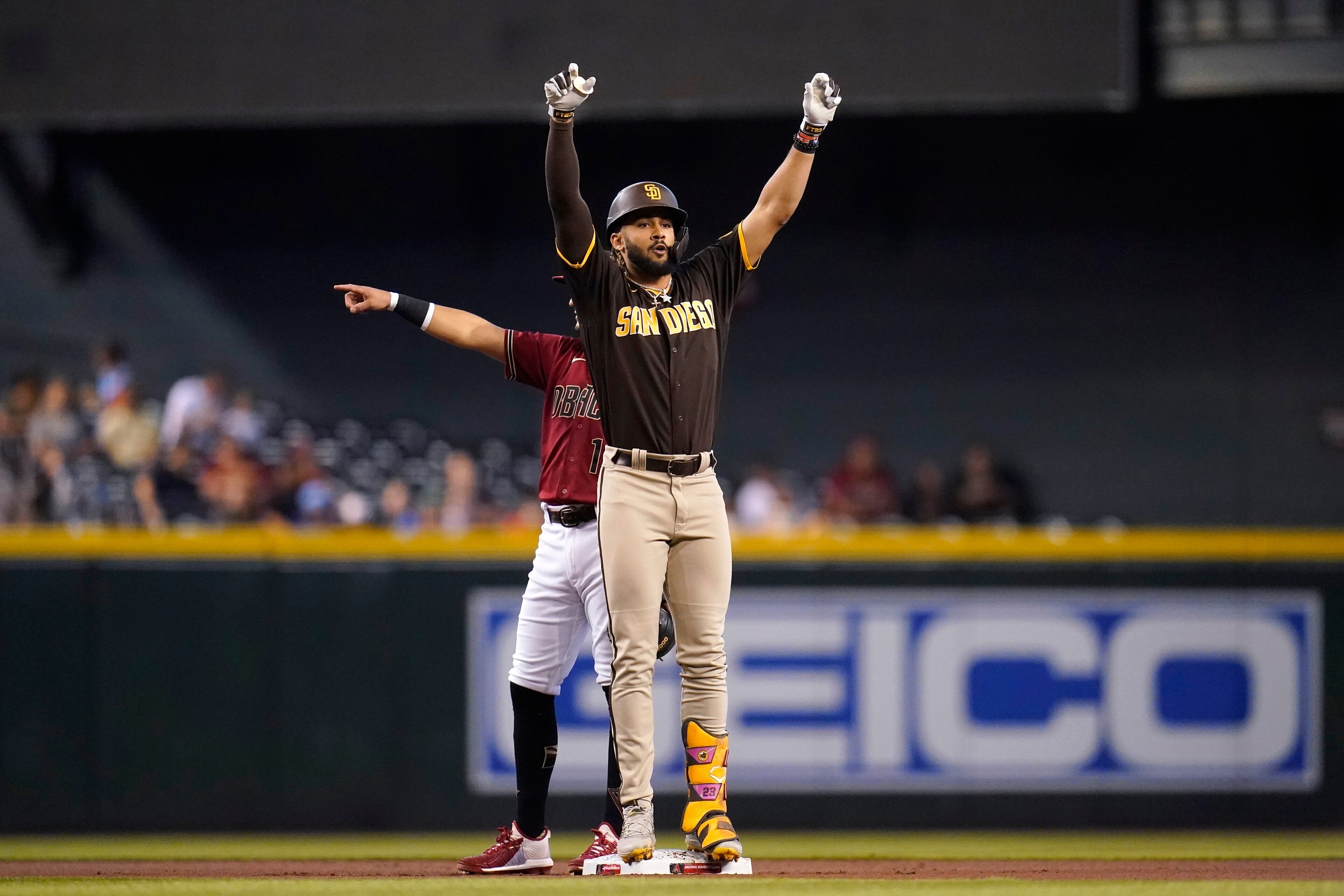 San Diego Padres' Fernando Tatis Jr., front, stands on second base as he celebrates his double and Arizona Diamondbacks second baseman Josh Rojas, back, points to a teammate during the first inning of a baseball game, Sunday, Aug. 15, 2021, in Phoenix. (AP Photo/Ross D. Franklin)