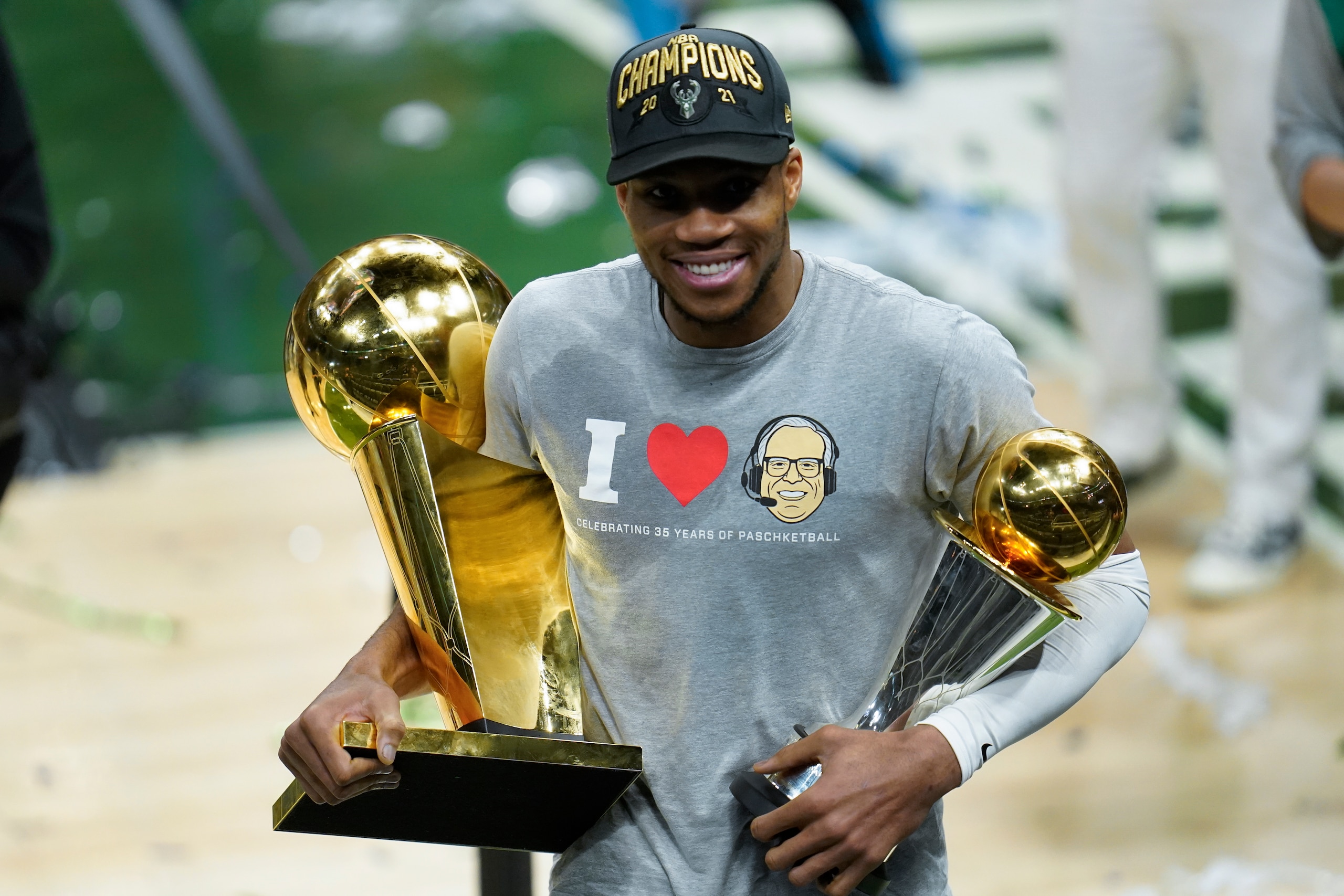 Milwaukee Bucks forward Giannis Antetokounmpo smiles while holding the championship trophy, left, and Most Valuable Player trophy after defeating the Phoenix Suns in Game 6 of basketball's NBA Finals in Milwaukee, Tuesday, July 20, 2021. The Bucks won 105-98. (AP Photo/Paul Sancya)