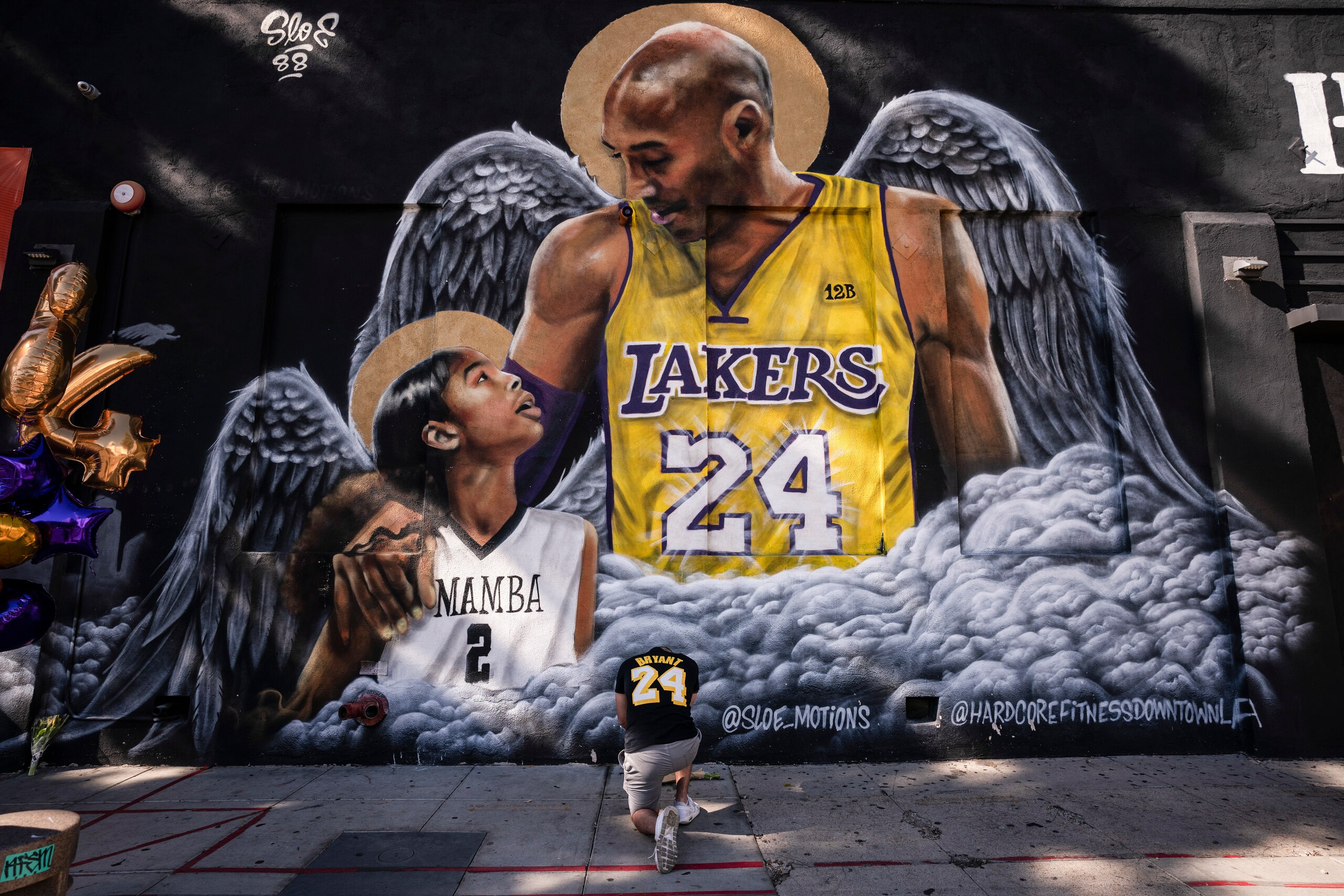 FILE - In this Jan. 26, 2021, file photo, Adam Dergazarian, bottom center, pays his respects for Kobe Bryant and his daughter, Gianna, in front of a mural painted by artist Louie Sloe Palsino in Los Angeles. Federal safety officials are expected to vote Tuesday, Feb. 9, 2021, on what likely caused the helicopter carrying Kobe Bryant, his 13-year-old daughter and seven others to crash into a Southern California hillside last year, killing all aboard. (AP Photo/Jae C. Hong, File) FILE - In this Jan. 26, 2021, file photo, Adam Dergazarian, bottom center, pays his respects for Kobe Bryant and his daughter, Gianna, in front of a mural painted by artist Louie Sloe Palsino in Los Angeles. Federal safety officials are expected to vote Tuesday, Feb. 9, 2021, on what likely caused the helicopter carrying Kobe Bryant, his 13-year-old daughter and seven others to crash into a Southern California hillside last year, killing all aboard. (AP Photo/Jae C. Hong, File)