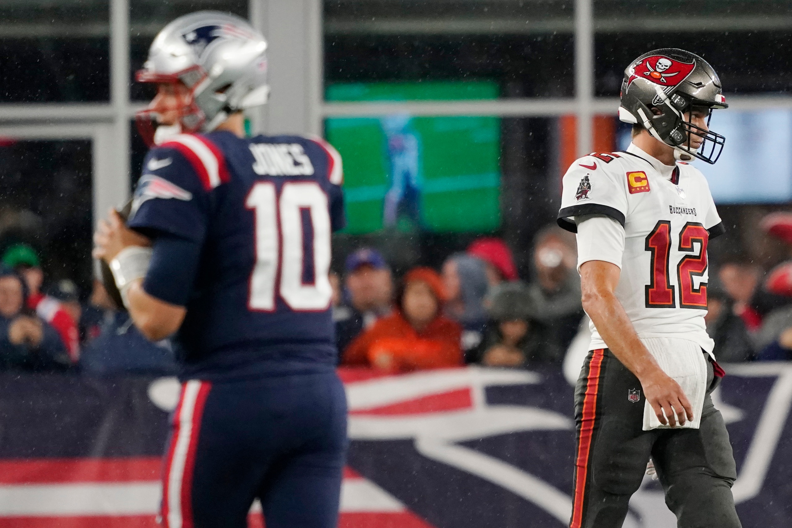 Tampa Bay Buccaneers quarterback Tom Brady (12) walks towards his bench as New England Patriots quarterback Mac Jones (10) warms up prior to an NFL football game between the New England Patriots and Tampa Bay Buccaneers, Sunday, Oct. 3, 2021, in Foxborough, Mass. (AP Photo/Elise Amendola)