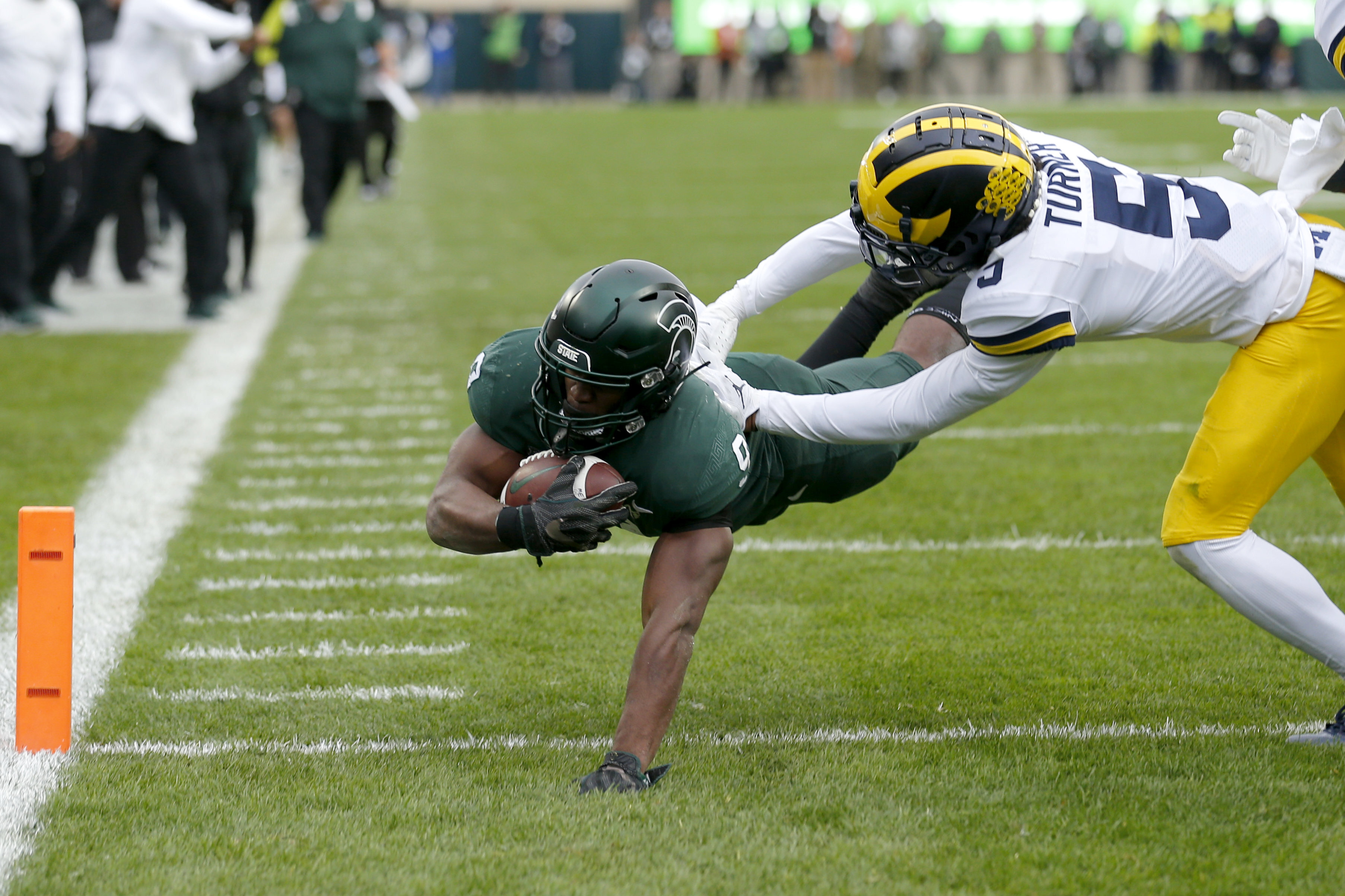 Michigan State's Kenneth Walker III, left, dives over the goal line for a touchdown against Michigan's DJ Turner during the second quarter of an NCAA college football game, Saturday, Oct. 30, 2021, in East Lansing, Mich. (AP Photo/Al Goldis)