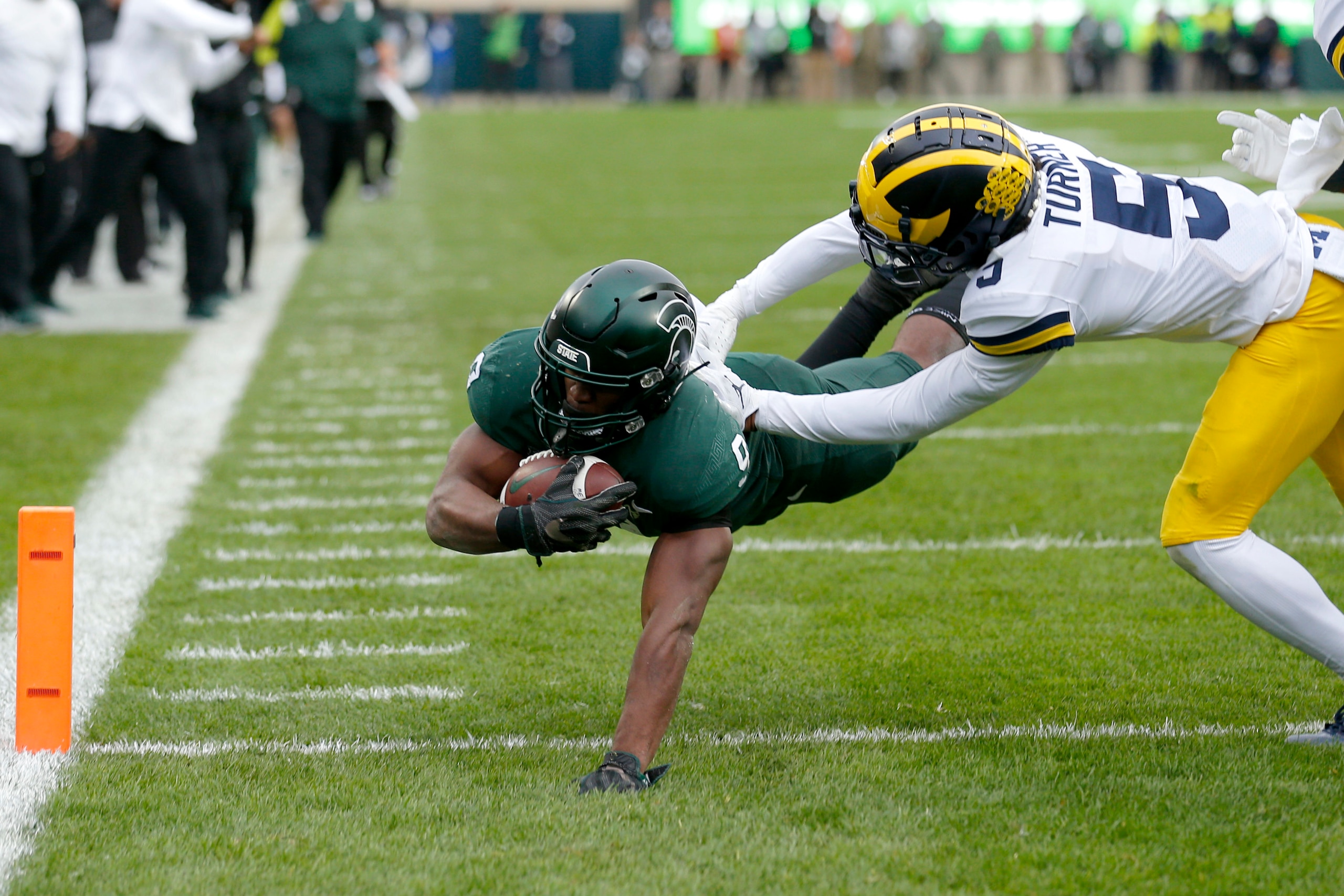 Michigan State's Kenneth Walker III, left, dives over the goal line for a touchdown against Michigan's DJ Turner during the second quarter of an NCAA college football game, Saturday, Oct. 30, 2021, in East Lansing, Mich. (AP Photo/Al Goldis)