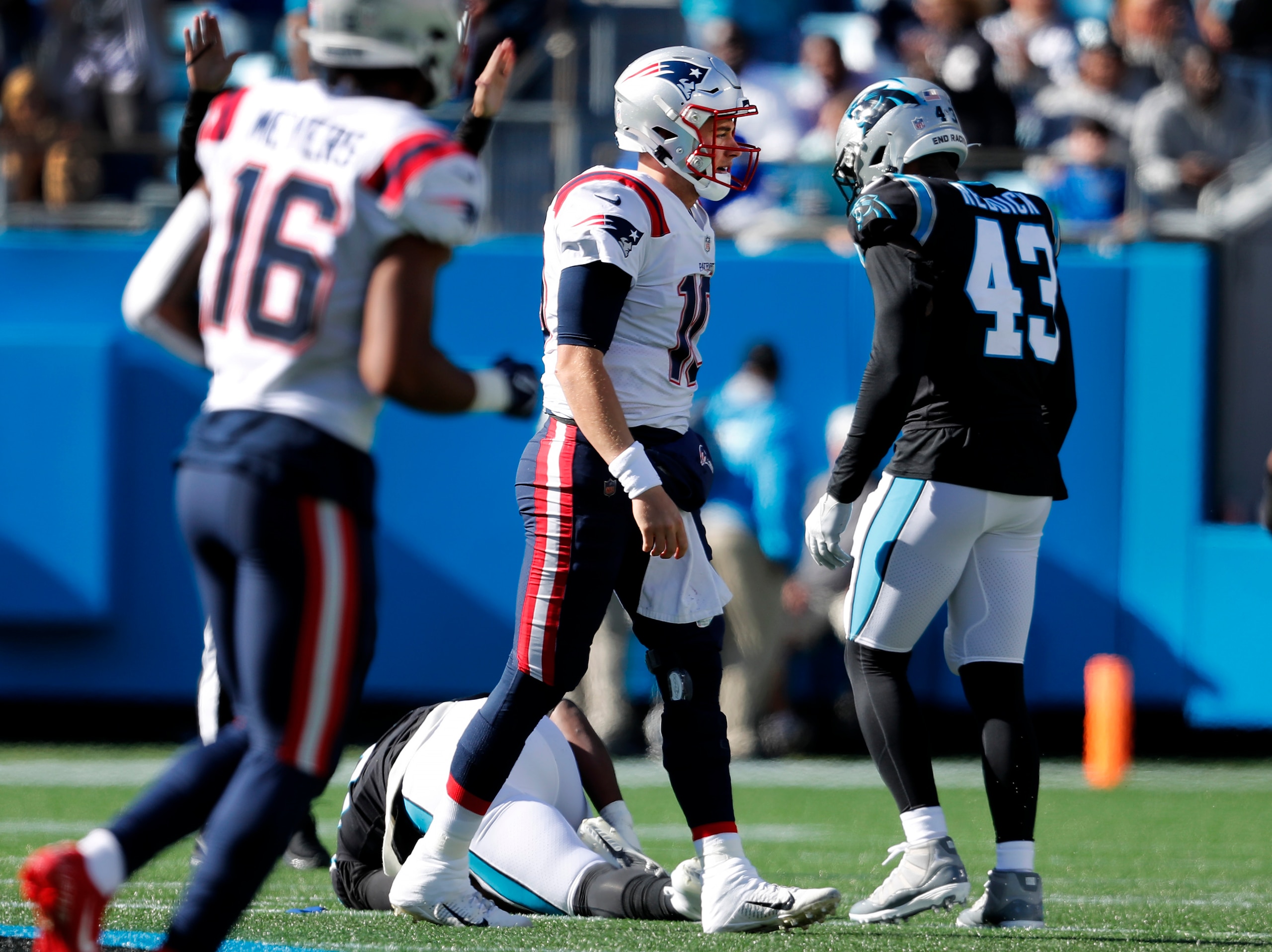 Charlotte, NC - November 7: Patriots quarterback Mac Jones walks off the field with Panthers DE Brian Burns, who is injured on the ground in the background. Carolina's LB Haason Reddick (43) is at right. Burns was injured on the play in which Jones fumbled and the Panthers recovered. After the game, Reddick accused Jones of a dirty play on Burns. The New England Patriots visited the Carolina Panthers for a regular season NFL football game at Bank of America Stadium in Charlotte, NC on Nov. 7, 2021. (Photo by Jim Davis/The Boston Globe via Getty Images)