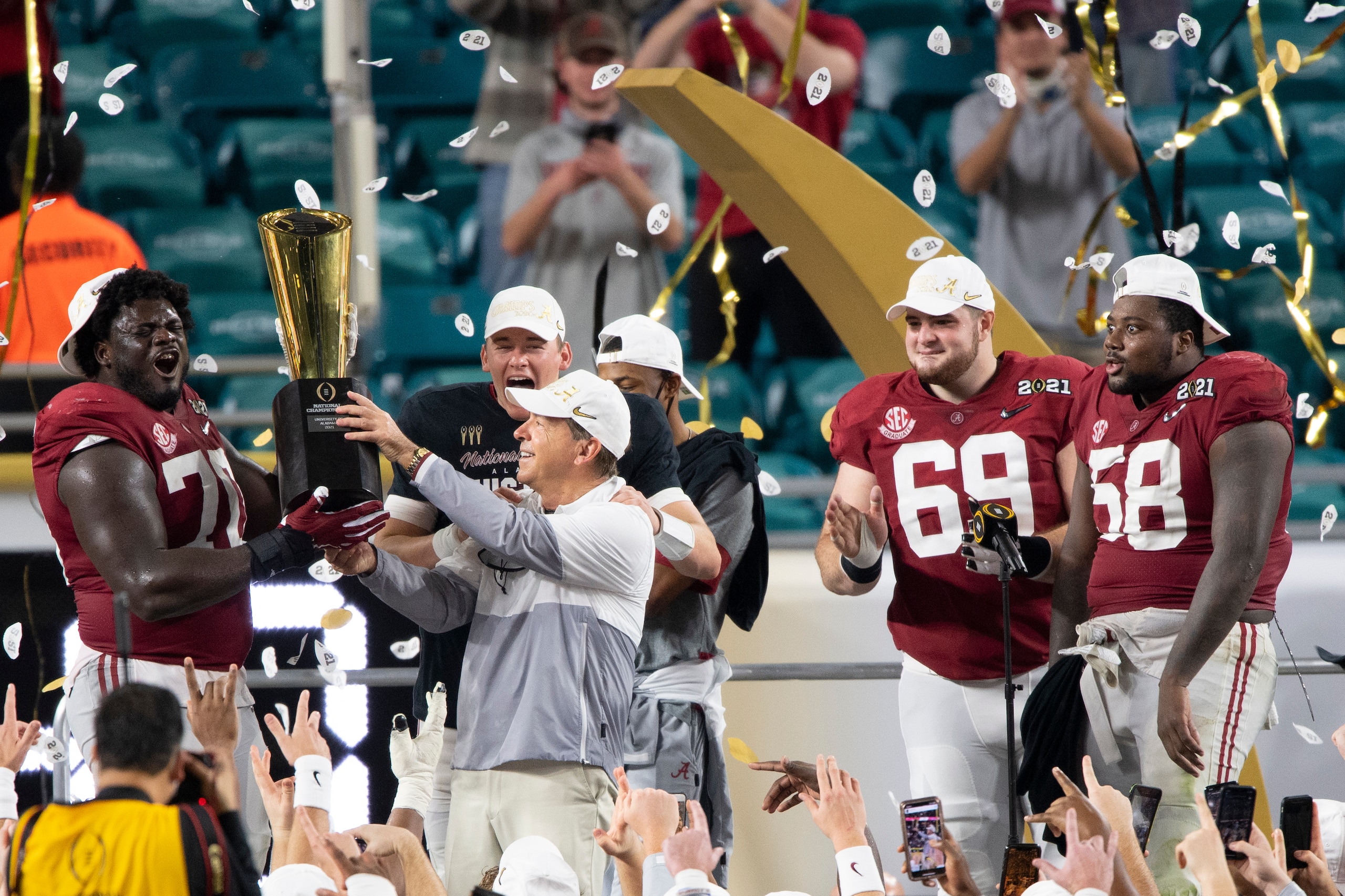 MIAMI GARDENS, FL - JANUARY 11: Alabama Crimson Tide offensive lineman Alex Leatherwood (70) and Alabama Crimson Tide head coach Nick Saban hold the trophy as they celebrate on the stage with Alabama Crimson Tide quarterback Mac Jones (10), Alabama Crimson Tide wide receiver DeVonta Smith (6), Alabama Crimson Tide offensive lineman Landon Dickerson (69) and Alabama Crimson Tide defensive lineman Christian Barmore (58) after the Alabama Crimson Tide defeated the Ohio State Buckeyes at the College Football Playoff National Championship football game on January 11, 2021 at the Hard Rock Stadium in Miami Gardens, FL. (Photo by Doug Murray/Icon Sportswire via Getty Images)
