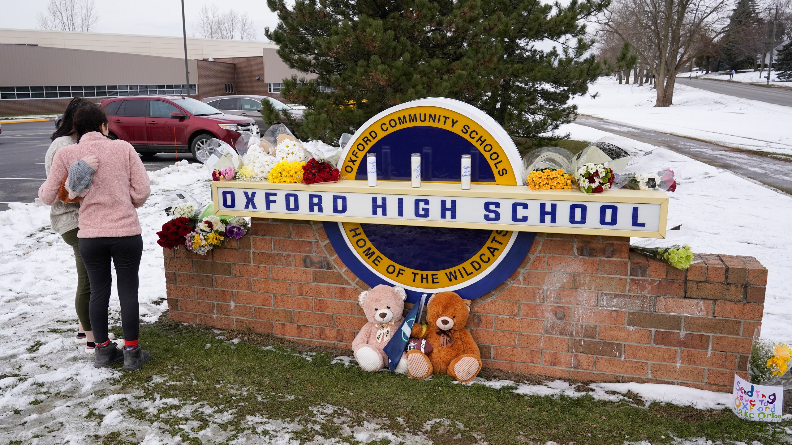 Students stand at the sign of Oxford High School where memorial items are being placed in Oxford, Mich., Wednesday, Dec. 1, 2021. A 15-year-old sophomore opened fire at the school, killing several students and wounding multiple other people, including a teacher. (AP Photo/Paul Sancya)