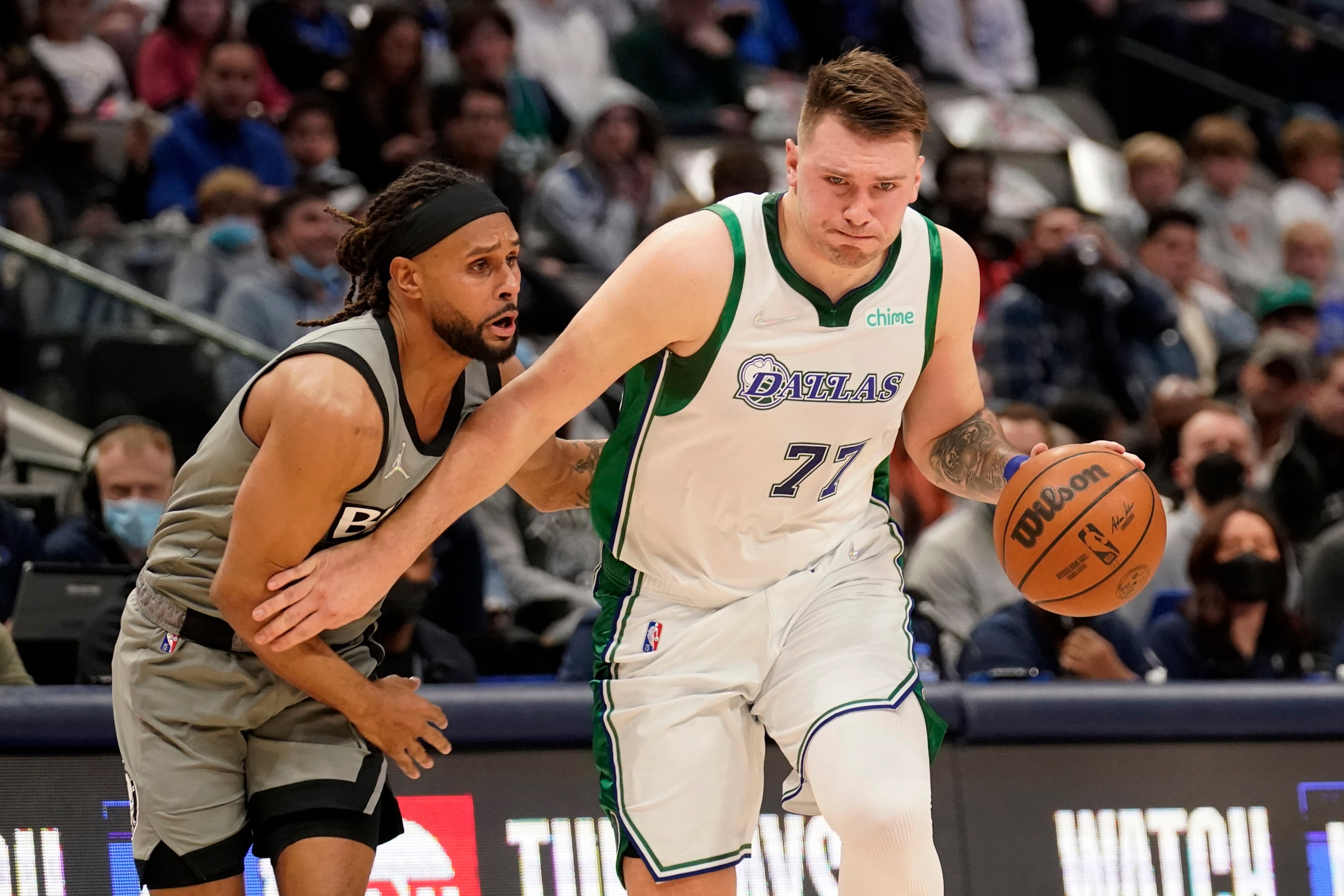 Brooklyn Nets guard Patty Mills, left, defends as Dallas Mavericks guard Luka Doncic (77) moves to the basket in the first half of an NBA basketball game in Dallas, Tuesday, Dec. 7, 2021. (AP Photo/Tony Gutierrez)