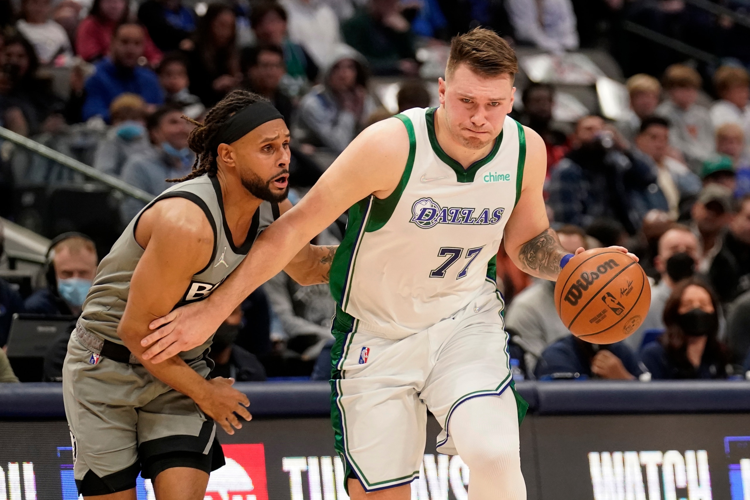 Brooklyn Nets guard Patty Mills, left, defends as Dallas Mavericks guard Luka Doncic (77) moves to the basket in the first half of an NBA basketball game in Dallas, Tuesday, Dec. 7, 2021. (AP Photo/Tony Gutierrez)