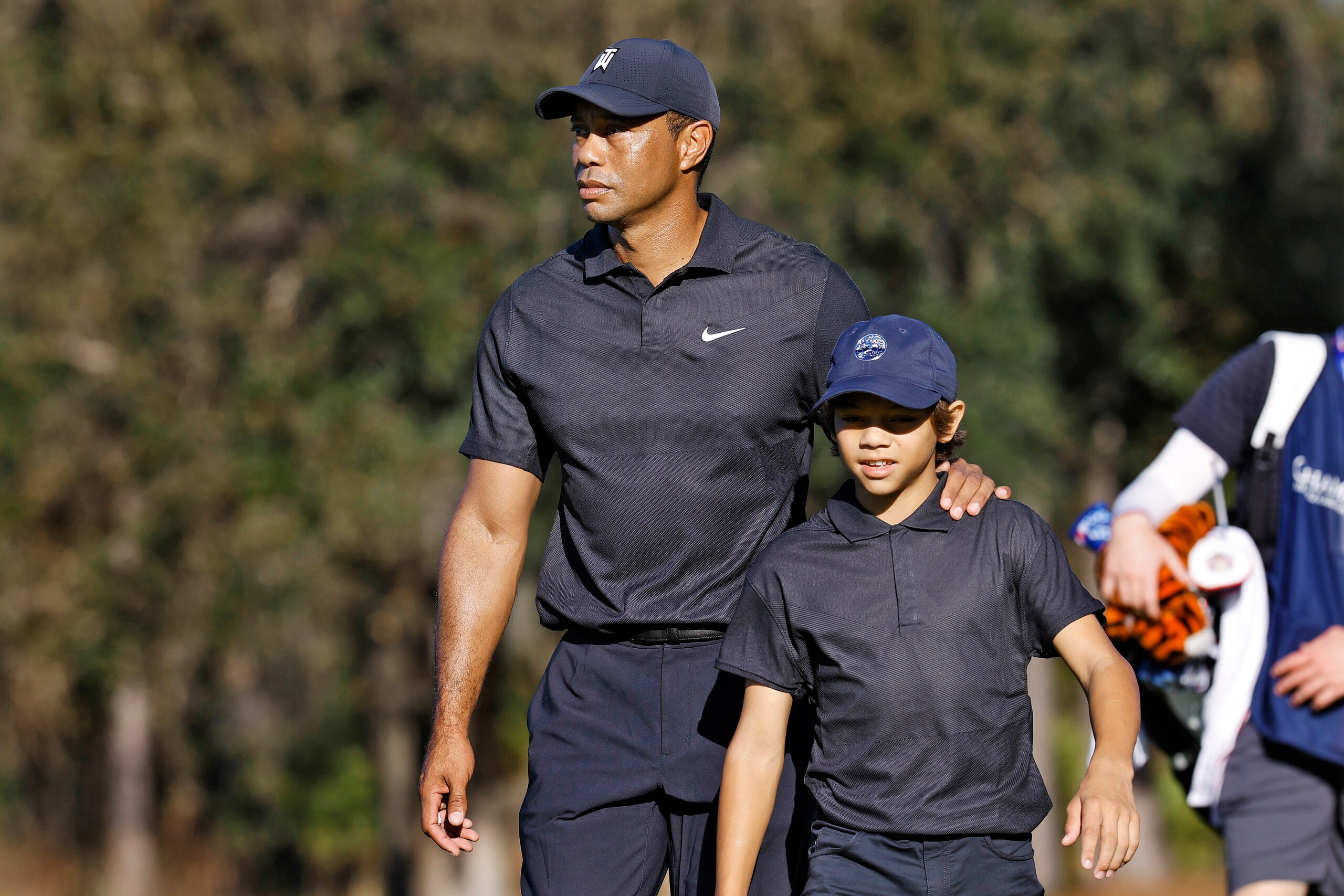 Tiger Woods, left, and his son Charlie walk the first fairway during the first round of the PNC Championship golf tournament Friday, Dec. 17, 2021, in Orlando, Fla. Woods is back playing after getting injured in a car accident. He is paired with Charlie during the tournament. (AP Photo/Scott Audette)
