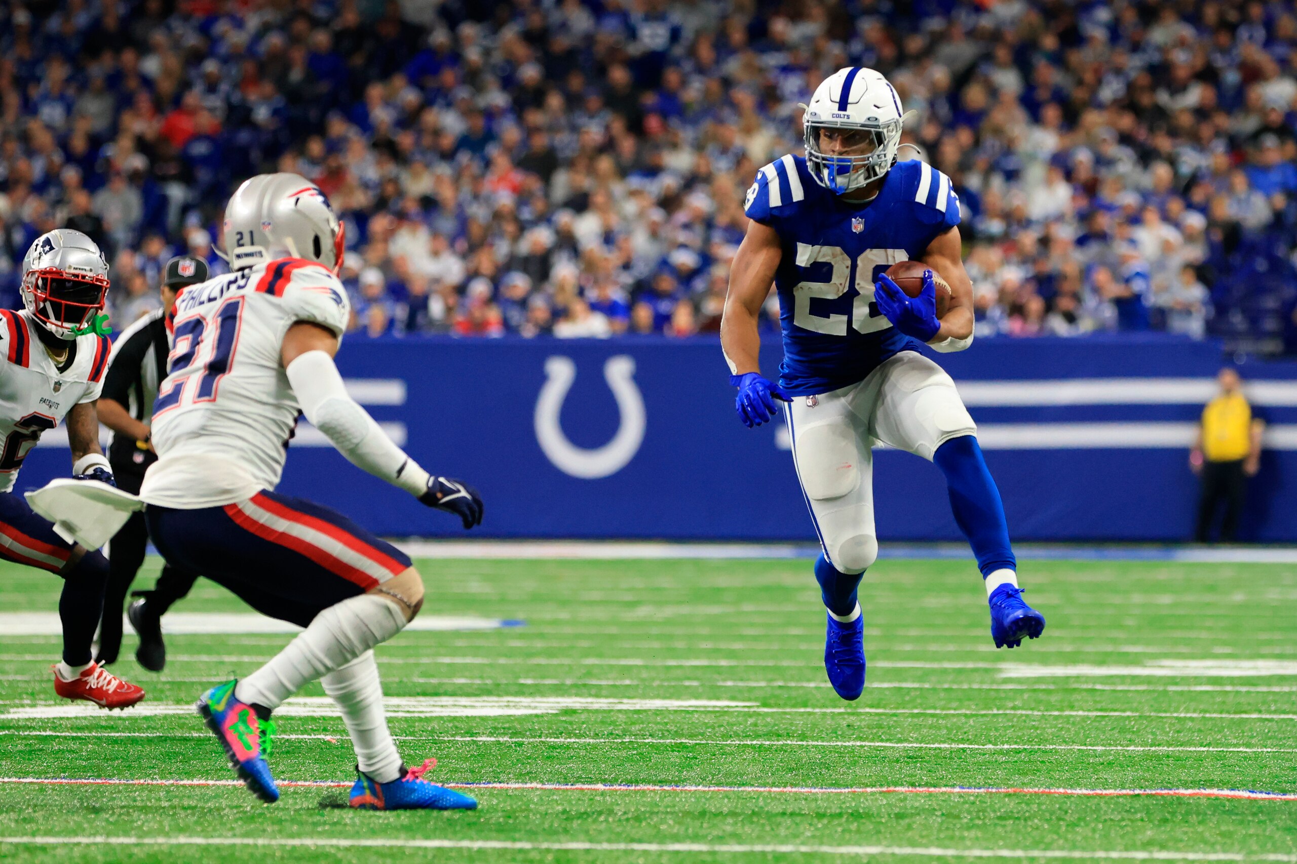 Indianapolis Colts running back Jonathan Taylor (28) runs with the ball as New England Patriots safety Adrian Phillips (21) defends during the first half of an NFL football game Saturday, Dec. 18, 2021, in Indianapolis. (AP Photo/Aaron Doster)