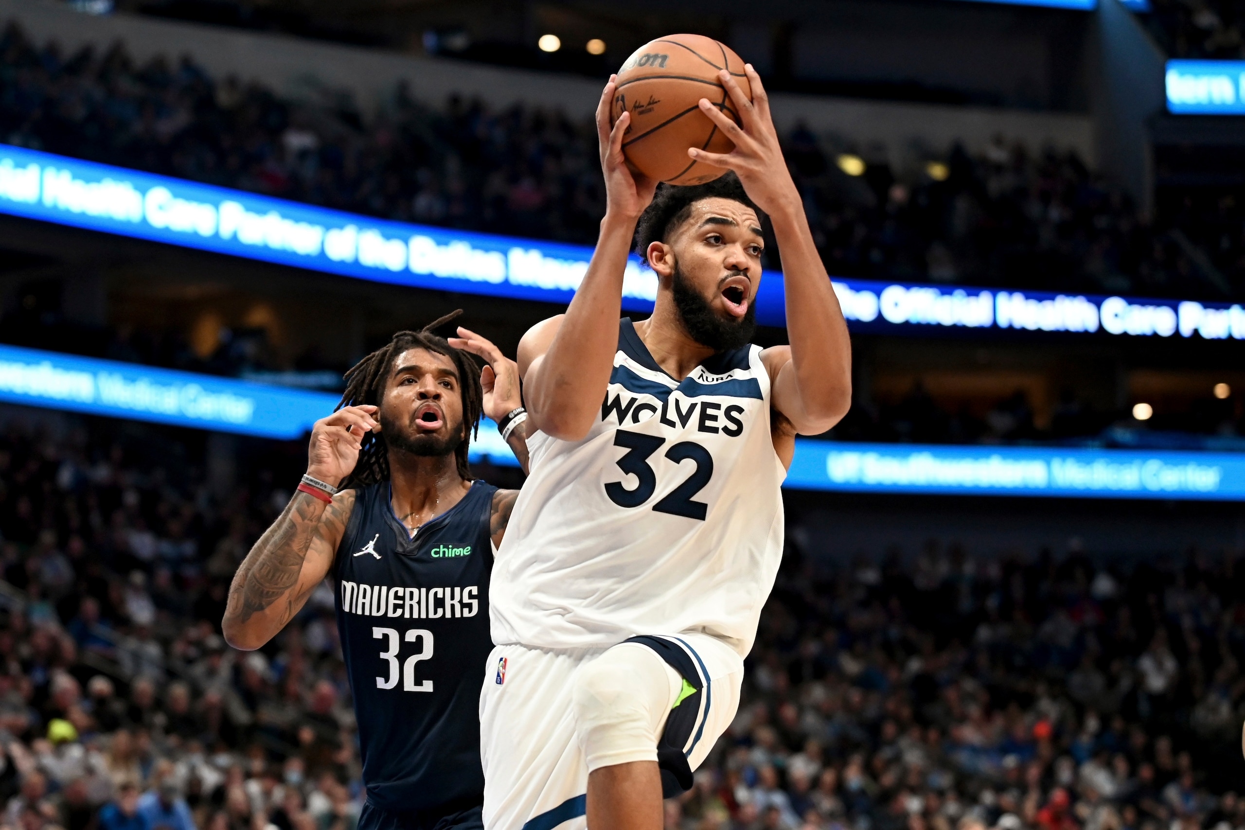 Minnesota Timberwolves center Karl-Anthony Towns, front, looks to make a pass in front of Dallas Mavericks forward Marquese Chriss, rear, in the second half of an NBA basketball game in Dallas, Tuesday, Dec. 21, 2021. (AP Photo/Matt Strasen)