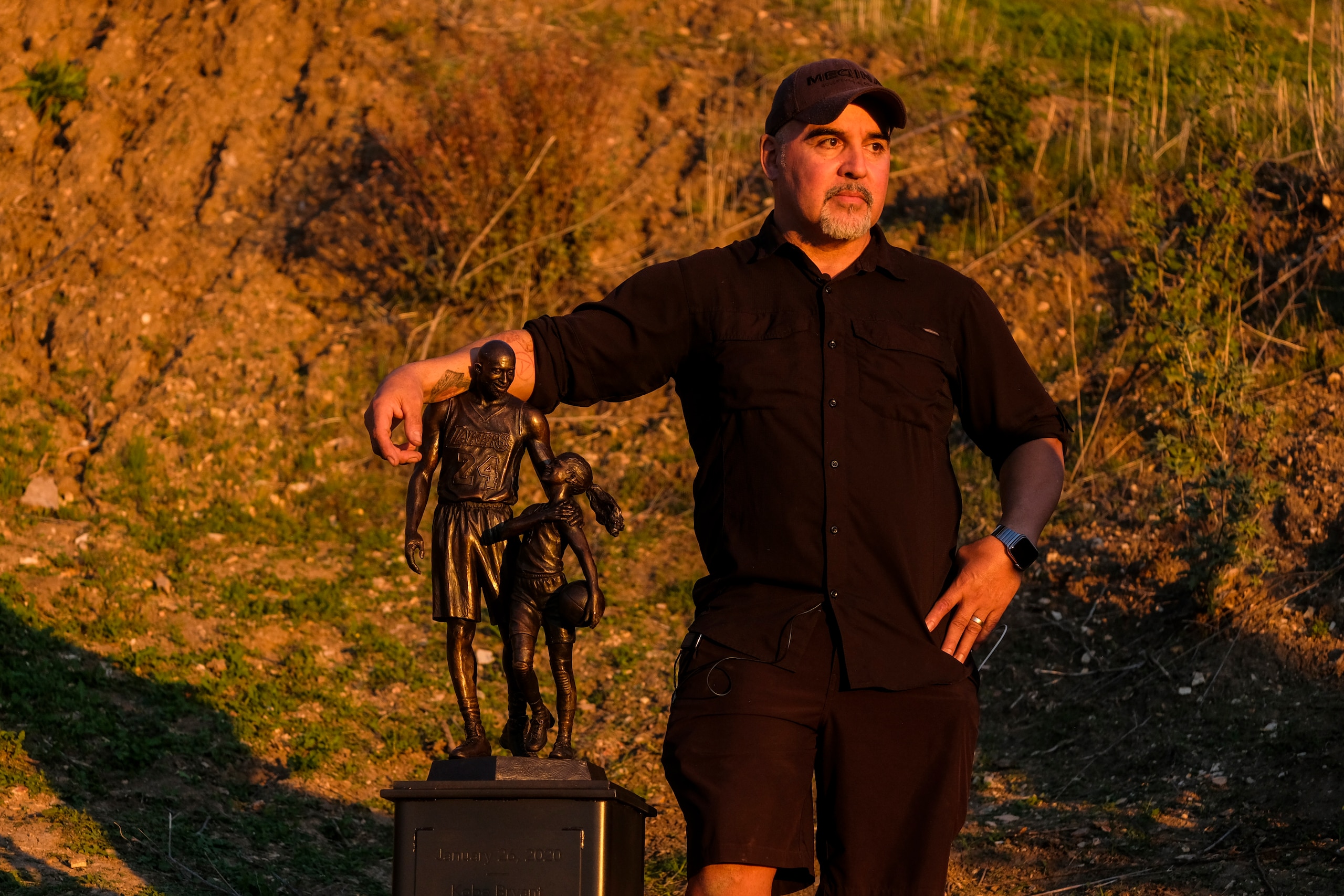 Artis Dan Medina stands next to his work, a bronze sculpture honoring former Los Angeles Lakers NBA basketball player Kobe Bryant, his daughter Gianna Bryant, and the names of those who died, at the site of a 2020 helicopter crash in Calabasas, Calif, on Wednesday, Jan. 26, 2022. (AP Photo/Ringo H.W. Chiu) Artis Dan Medina stands next to his work, a bronze sculpture honoring former Los Angeles Lakers NBA basketball player Kobe Bryant, his daughter Gianna Bryant, and the names of those who died, at the site of a 2020 helicopter crash in Calabasas, Calif, on Wednesday, Jan. 26, 2022. (AP Photo/Ringo H.W. Chiu)