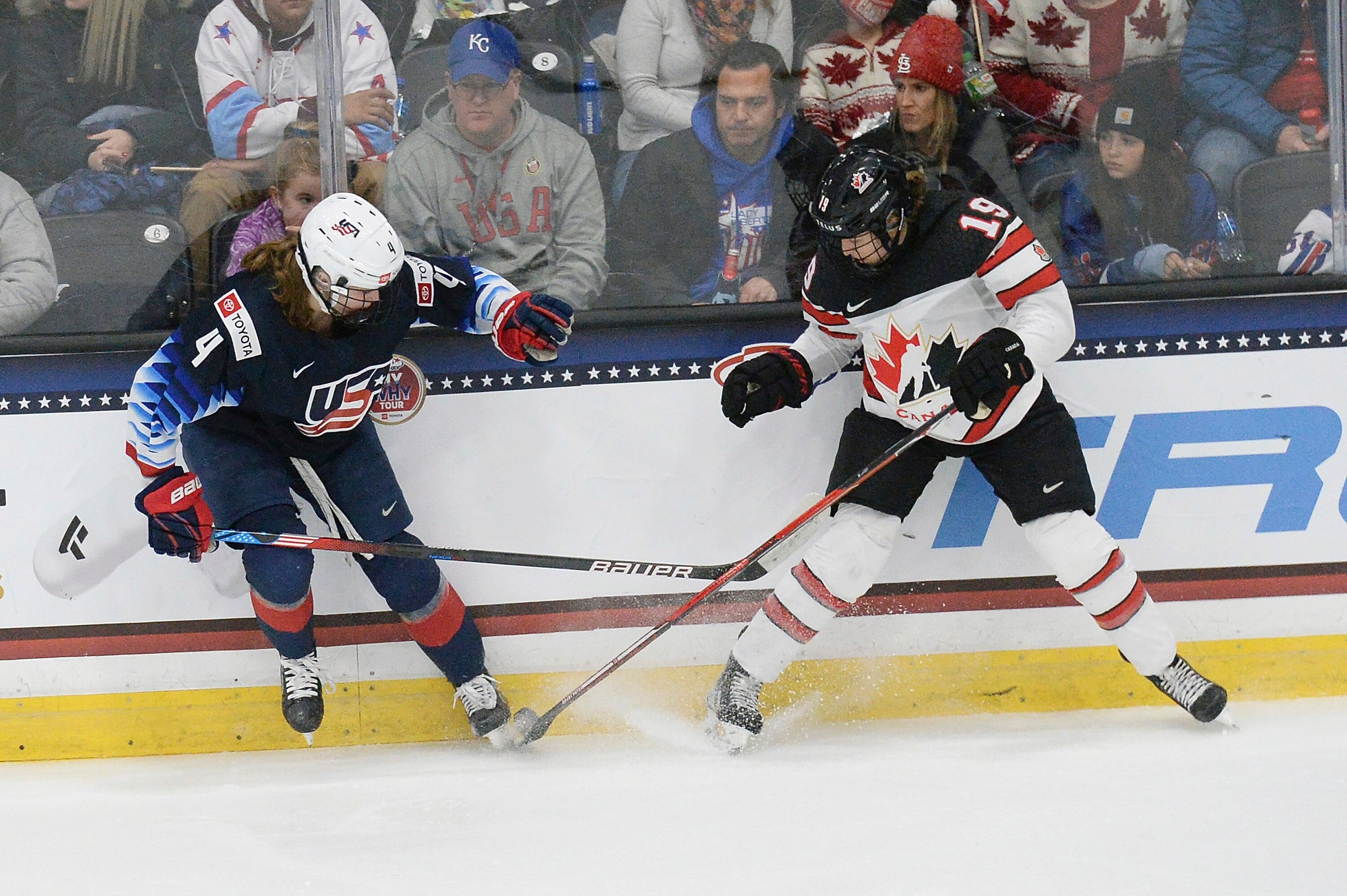 United States' Caroline Harvey (4) and Canada's Brianne Jenner (19) fight for the puck during the second period of a women's exhibition hockey game ahead of the Beijing Olympics, Friday, Dec. 17, 2021, in Maryland Heights, Mo. (AP Photo/Michael Thomas)