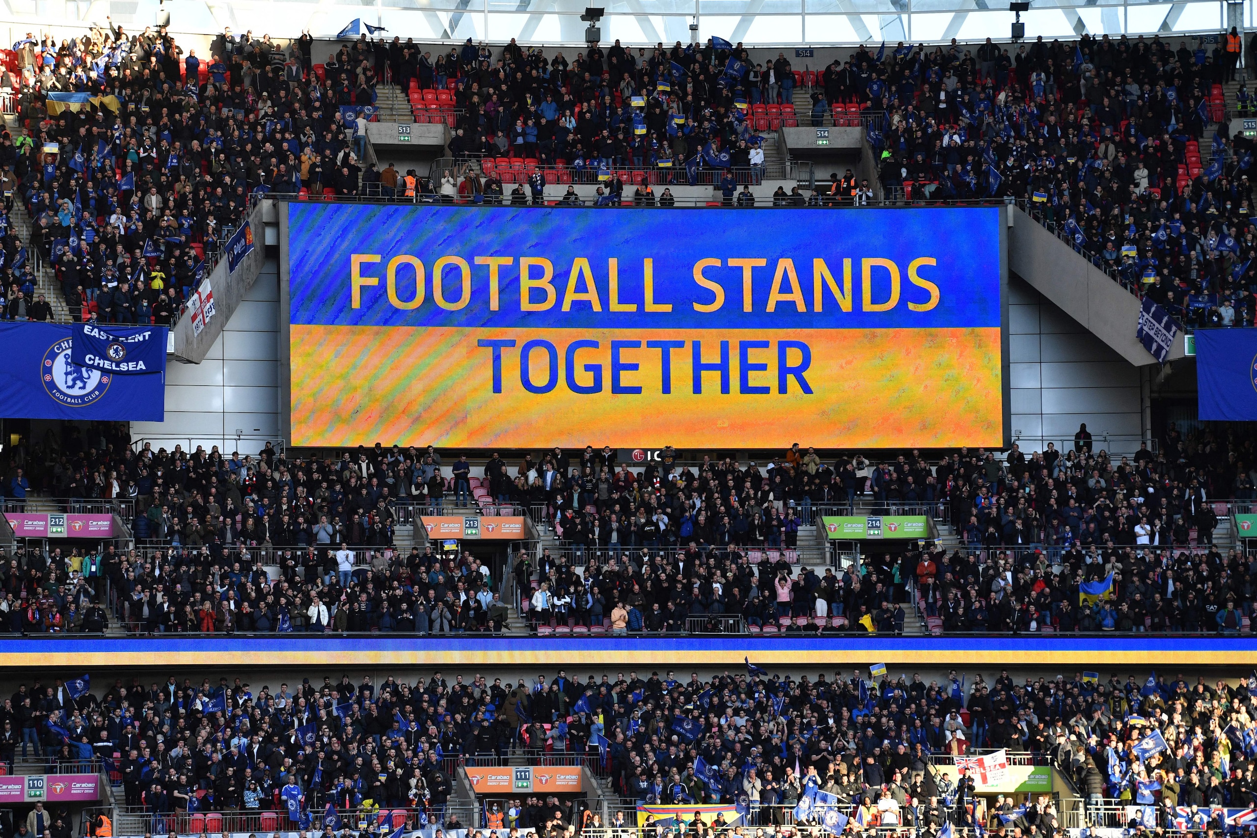 A 'Football Stands Together' message is displayed in Ukrainian colours ahead of the English League Cup final football match between Chelsea and Liverpool at Wembley Stadium, north-west London on February 27, 2022. - Russian billionaire Roman Abramovich handed over control of Chelsea to trustees of its charitable foundation on Saturday as Premier League players showed their support for war-torn Ukraine. - RESTRICTED TO EDITORIAL USE. No use with unauthorized audio, video, data, fixture lists, club/league logos or 'live' services. Online in-match use limited to 120 images. An additional 40 images may be used in extra time. No video emulation. Social media in-match use limited to 120 images. An additional 40 images may be used in extra time. No use in betting publications, games or single club/league/player publications. (Photo by JUSTIN TALLIS / AFP) / RESTRICTED TO EDITORIAL USE. No use with unauthorized audio, video, data, fixture lists, club/league logos or 'live' services. Online in-match use limited to 120 images. An additional 40 images may be used in extra time. No video emulation. Social media in-match use limited to 120 images. An additional 40 images may be used in extra time. No use in betting publications, games or single club/league/player publications. / RESTRICTED TO EDITORIAL USE. No use with unauthorized audio, video, data, fixture lists, club/league logos or 'live' services. Online in-match use limited to 120 images. An additional 40 images may be used in extra time. No video emulation. Social media in-match use limited to 120 images. An additional 40 images may be used in extra time. No use in betting publications, games or single club/league/player publications. (Photo by JUSTIN TALLIS/AFP via Getty Images)