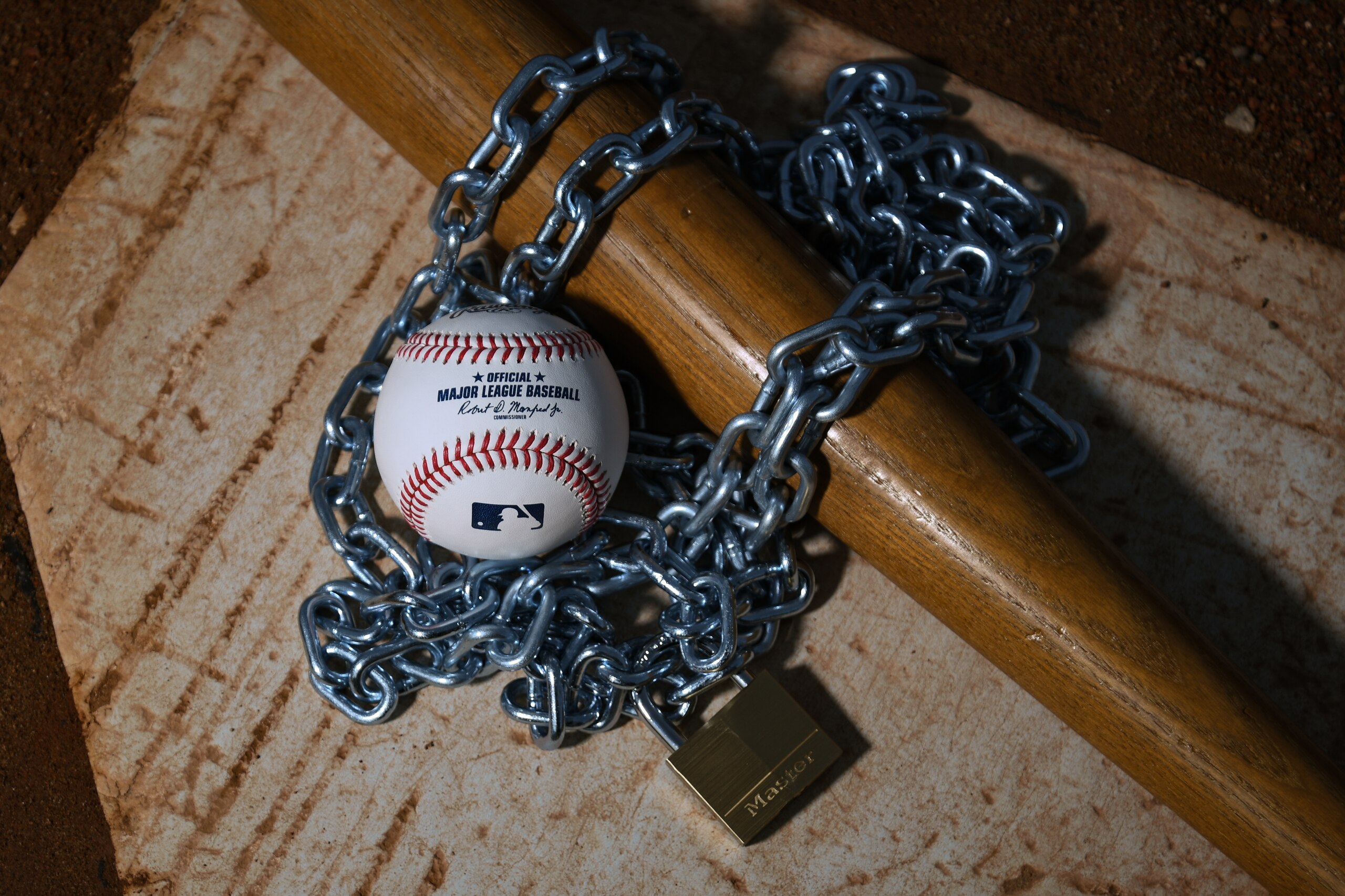 Brownsburg, IN - December 2: An Official Rawlings Major League Baseball sits with a bat, lock and chain to represent the lockout between Major League Baseball (MLB) and the Major League Baseball Players Association (MLBPA) on December 2, 2021 in Brownsburg, IN. (Photo by James Black/Icon Sportswire via Getty Images)