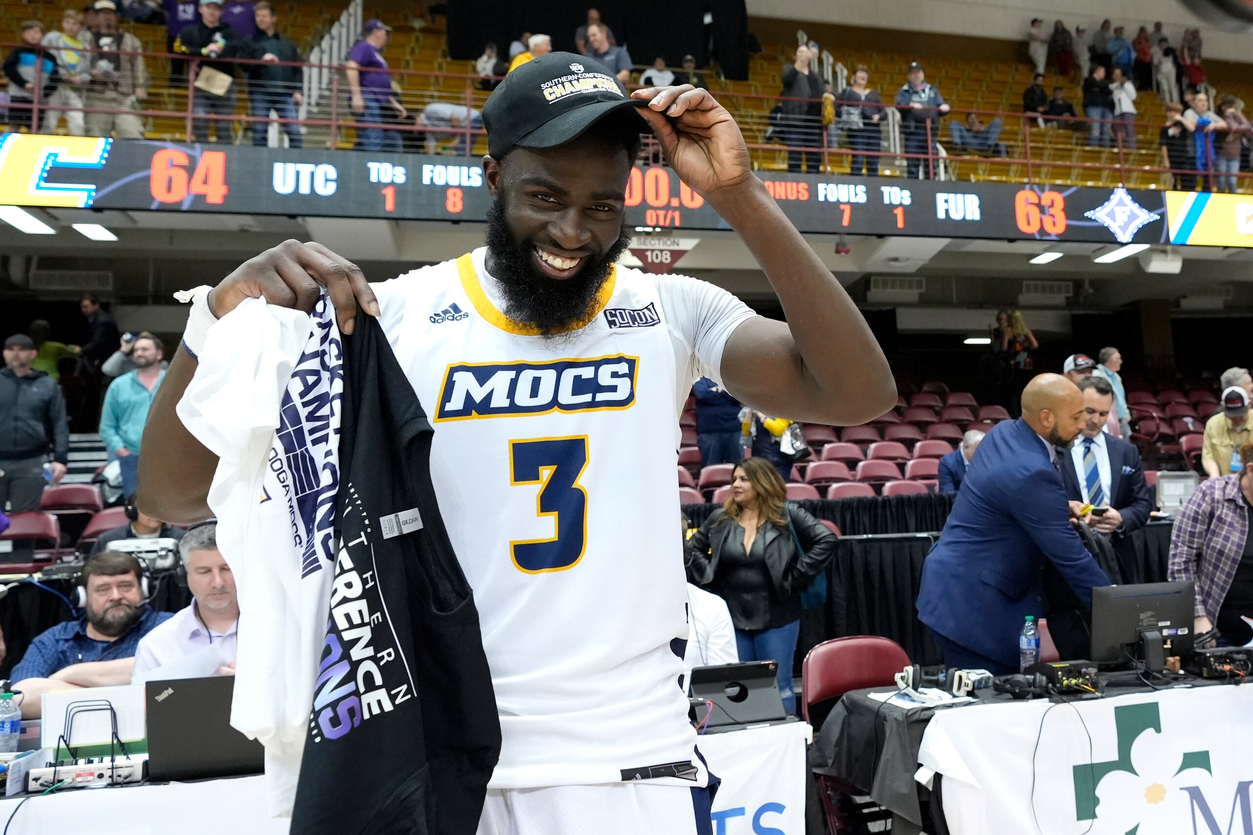 Chattanooga guard David Jean-Baptiste (3) puts on his championship cap after shooting the winning basket to defeat Furman in an NCAA college basketball championship game for the Southern Conference tournament, Monday, March 7, 2022, in Asheville, N.C. (AP Photo/Kathy Kmonicek)