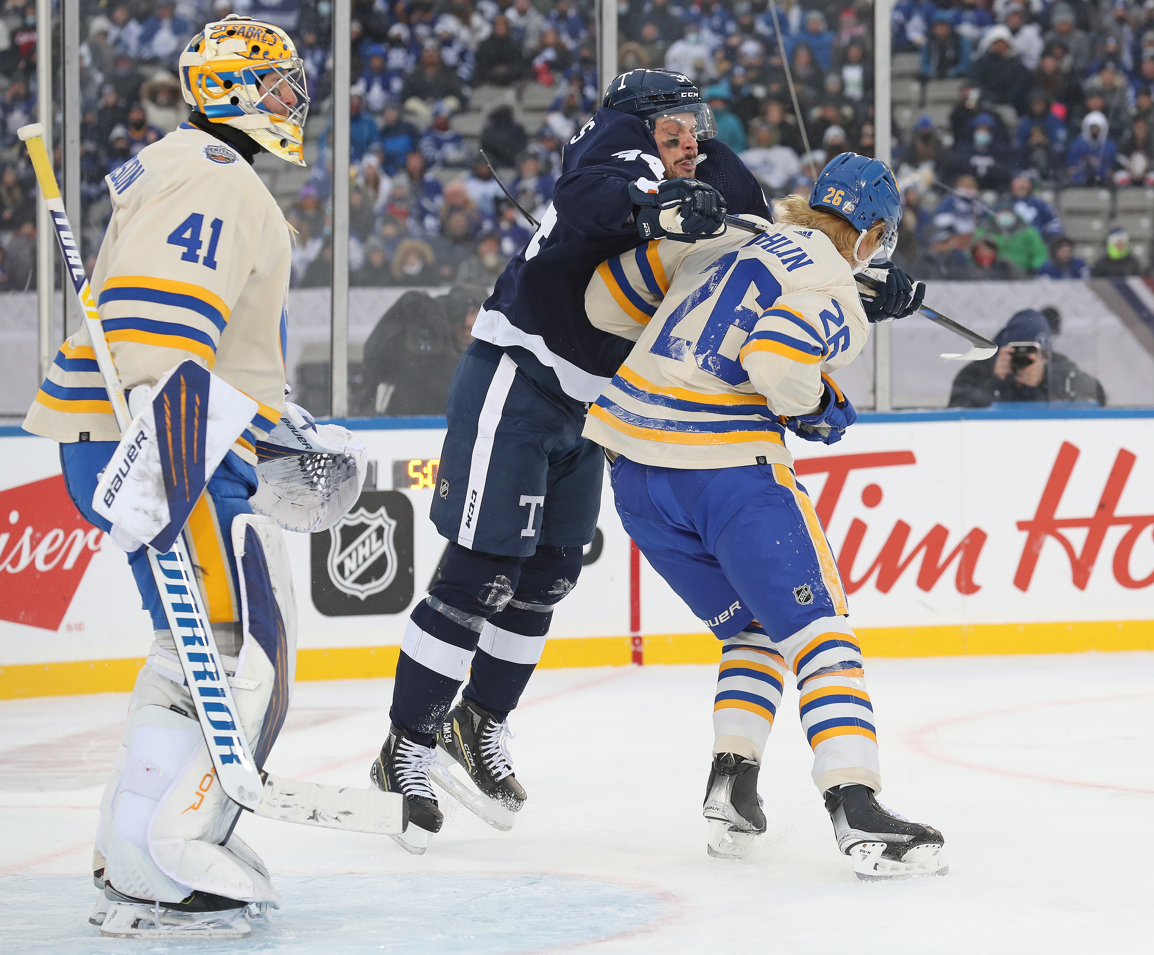 HAMILTON, ON - MARCH 13:  Auston Matthews #34 of the Toronto Maple Leafs cross checks Rasmus Dahlin #26 of the Buffalo Sabres in the 2022 Tim Hortons NHL Heritage Classic at Tim Hortons Field on March 13, 2022 in Hamilton, Ontario, Canada. The Sabres defeated the Maple Leafs 5-2. (Photo by Claus Andersen/Getty Images)