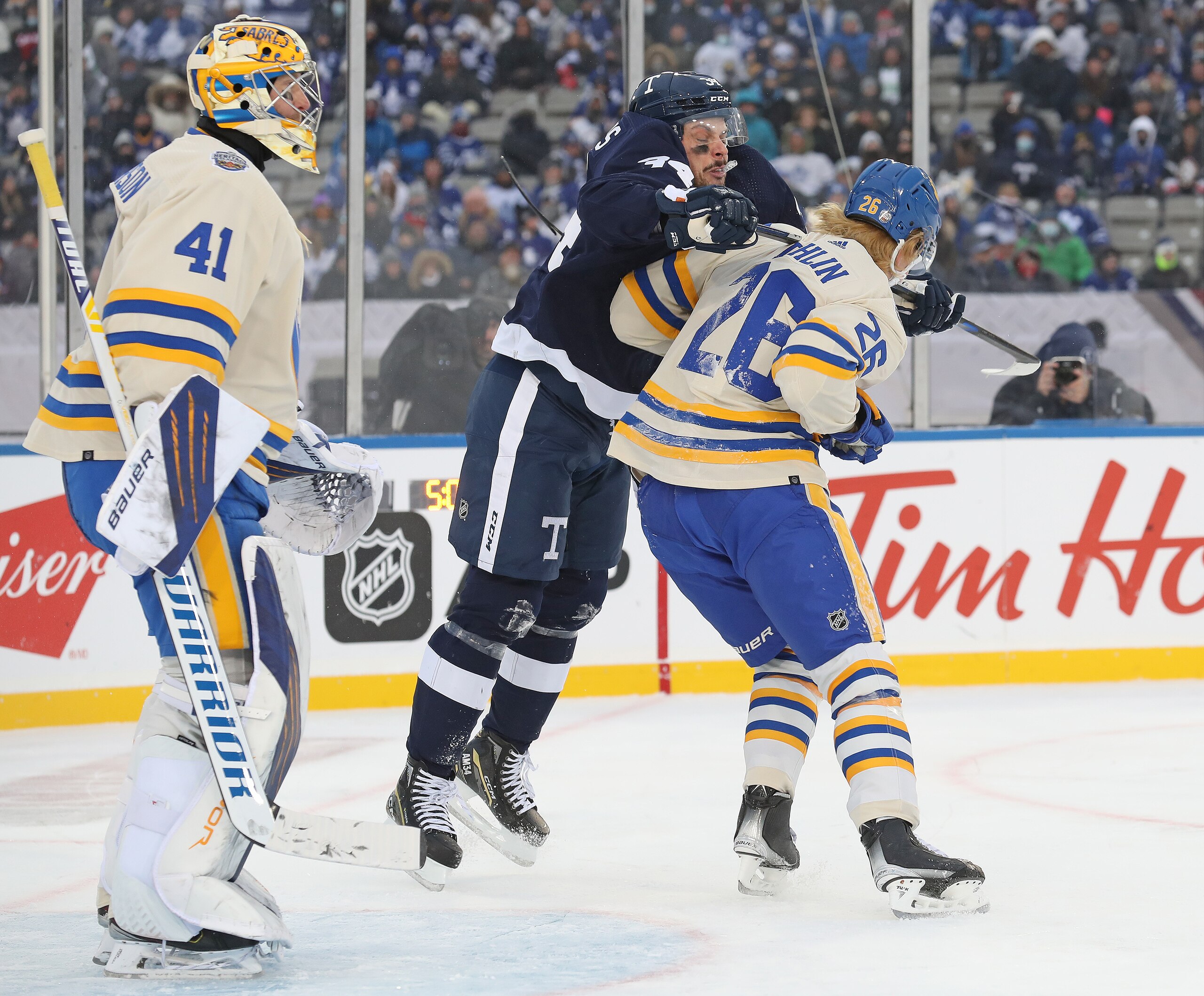 HAMILTON, ON - MARCH 13:  Auston Matthews #34 of the Toronto Maple Leafs cross checks Rasmus Dahlin #26 of the Buffalo Sabres in the 2022 Tim Hortons NHL Heritage Classic at Tim Hortons Field on March 13, 2022 in Hamilton, Ontario, Canada. The Sabres defeated the Maple Leafs 5-2. (Photo by Claus Andersen/Getty Images)