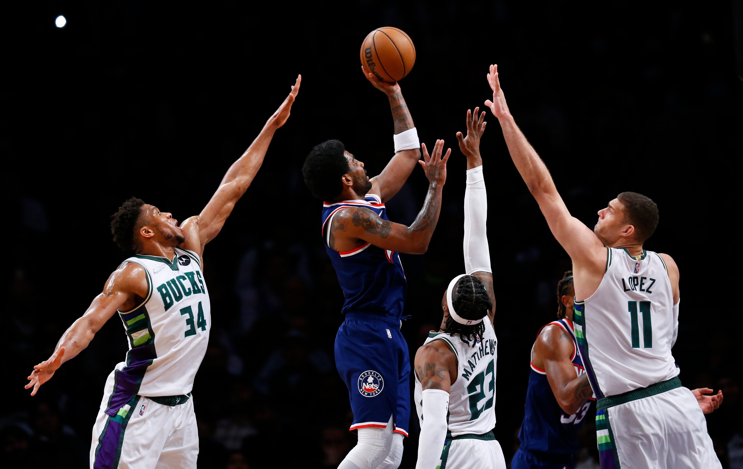 Brooklyn Nets guard Kyrie Irving (11) shoots from between Milwaukee Bucks' Giannis Antetokounmpo (34), Wesley Matthews (23) and Brook Lopez (11) during the first half of an NBA basketball game Thursday, March 31, 2022, in New York. (AP Photo/Noah K. Murray)