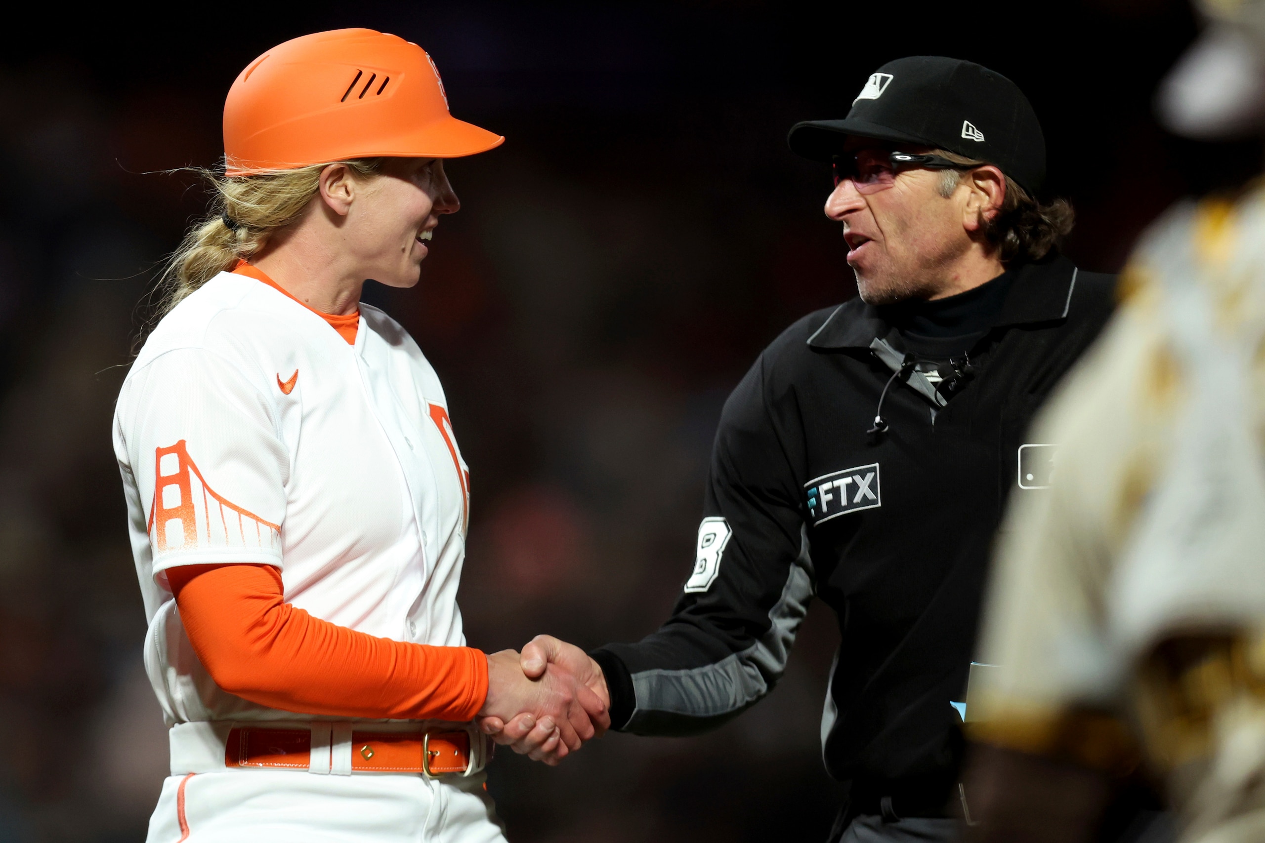 Home plate umpire Chris Guccione, right, shakes hands with San Francisco Giants first base coach Alyssa Nakken, left, against the San Diego Padres during a baseball game in San Francisco, Tuesday, April 12, 2022. (AP Photo/Jed Jacobsohn)