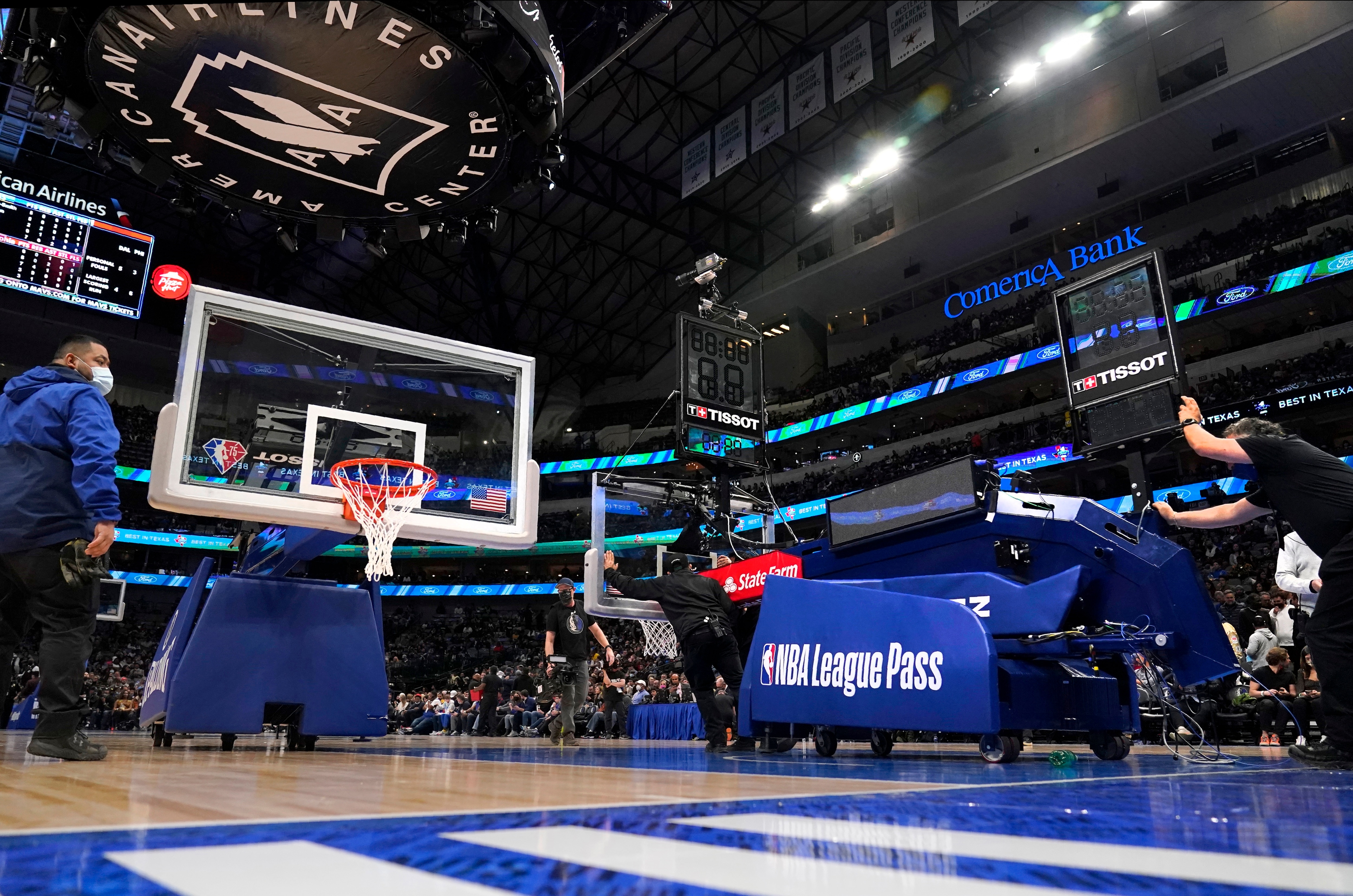Employees at American Airlines Center prepare to install a new rim, board and stanchion, left, after a mechanical difficulty with the one that had been used, right, during the first half of an NBA basketball game between the Philadelphia 76ers and the Dallas Mavericks in Dallas, Friday, Feb. 4, 2022. (AP Photo/Tony Gutierrez)