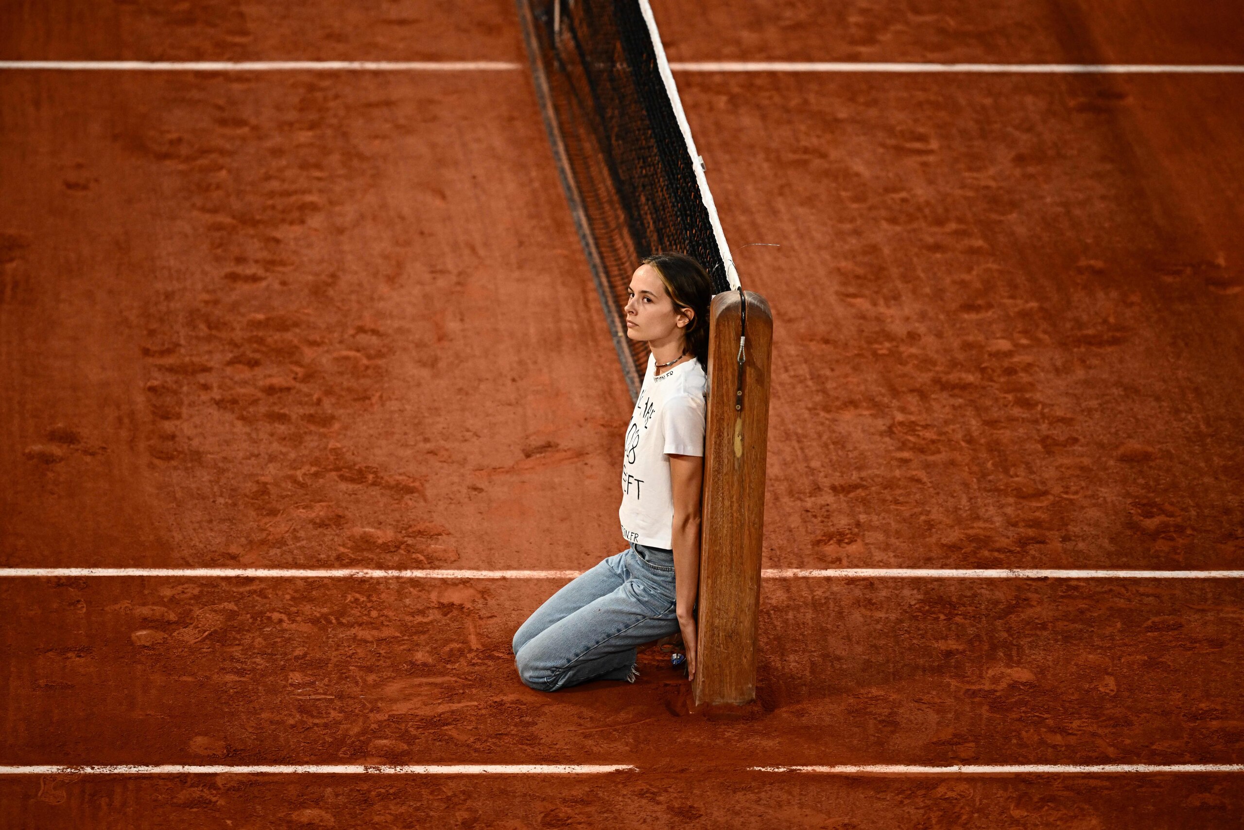 An activist kneels on court after attaching herself to the tennis net during the men's semi-final singles match between Norway's Casper Ruud and Croatia's Marin Cilic on day thirteen of the Roland-Garros Open tennis tournament at the Court Philippe-Chatrier in Paris on June 3, 2022. (Photo by Anne-Christine POUJOULAT / AFP) (Photo by ANNE-CHRISTINE POUJOULAT/AFP via Getty Images)