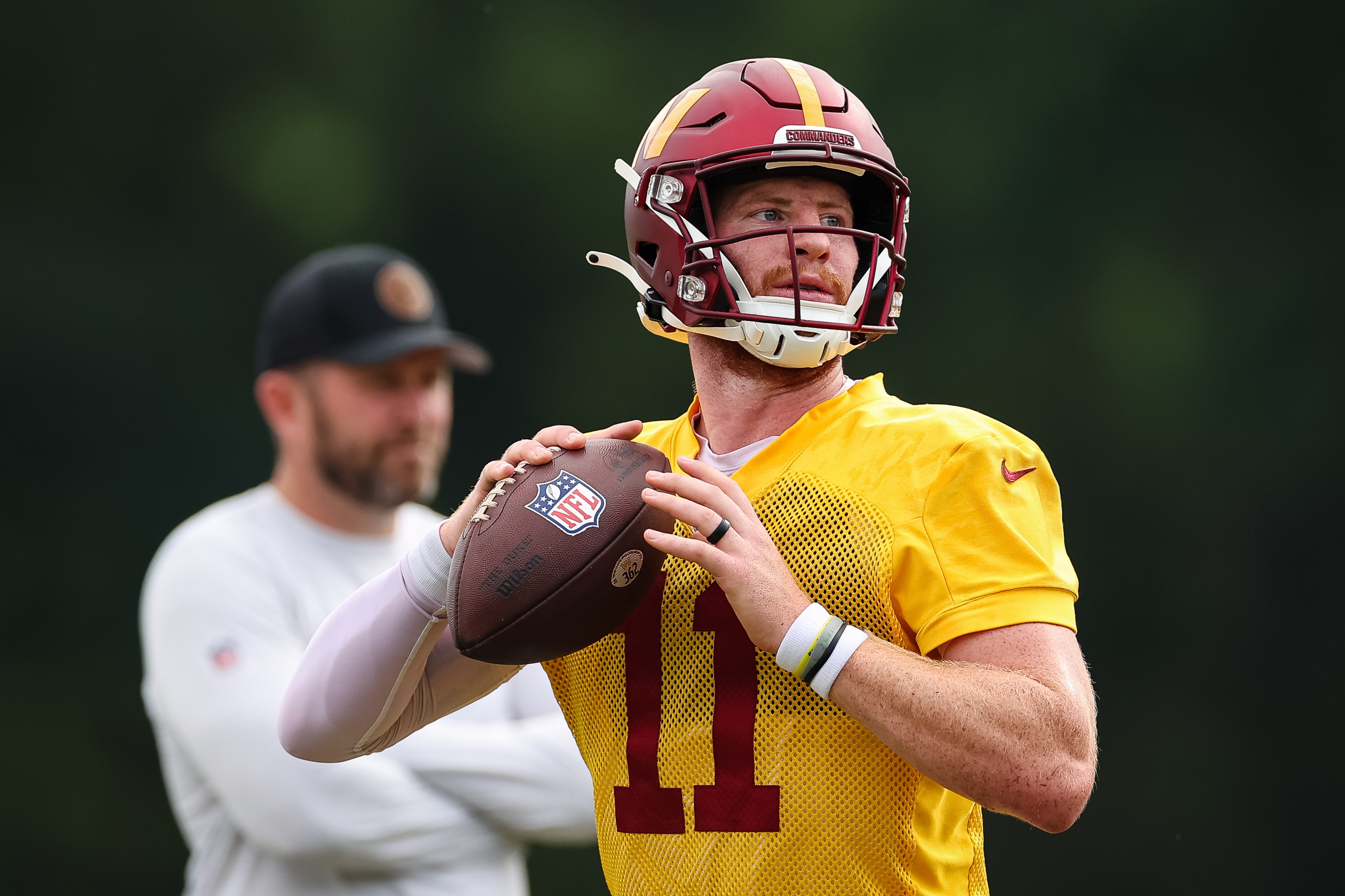 ASHBURN, VA - JUNE 08: Carson Wentz #11 of the Washington Commanders participates in a drill as offensive coordinator Scott Turner looks on during the organized team activity at INOVA Sports Performance Center on June 8, 2022 in Ashburn, Virginia. (Photo by Scott Taetsch/Getty Images)