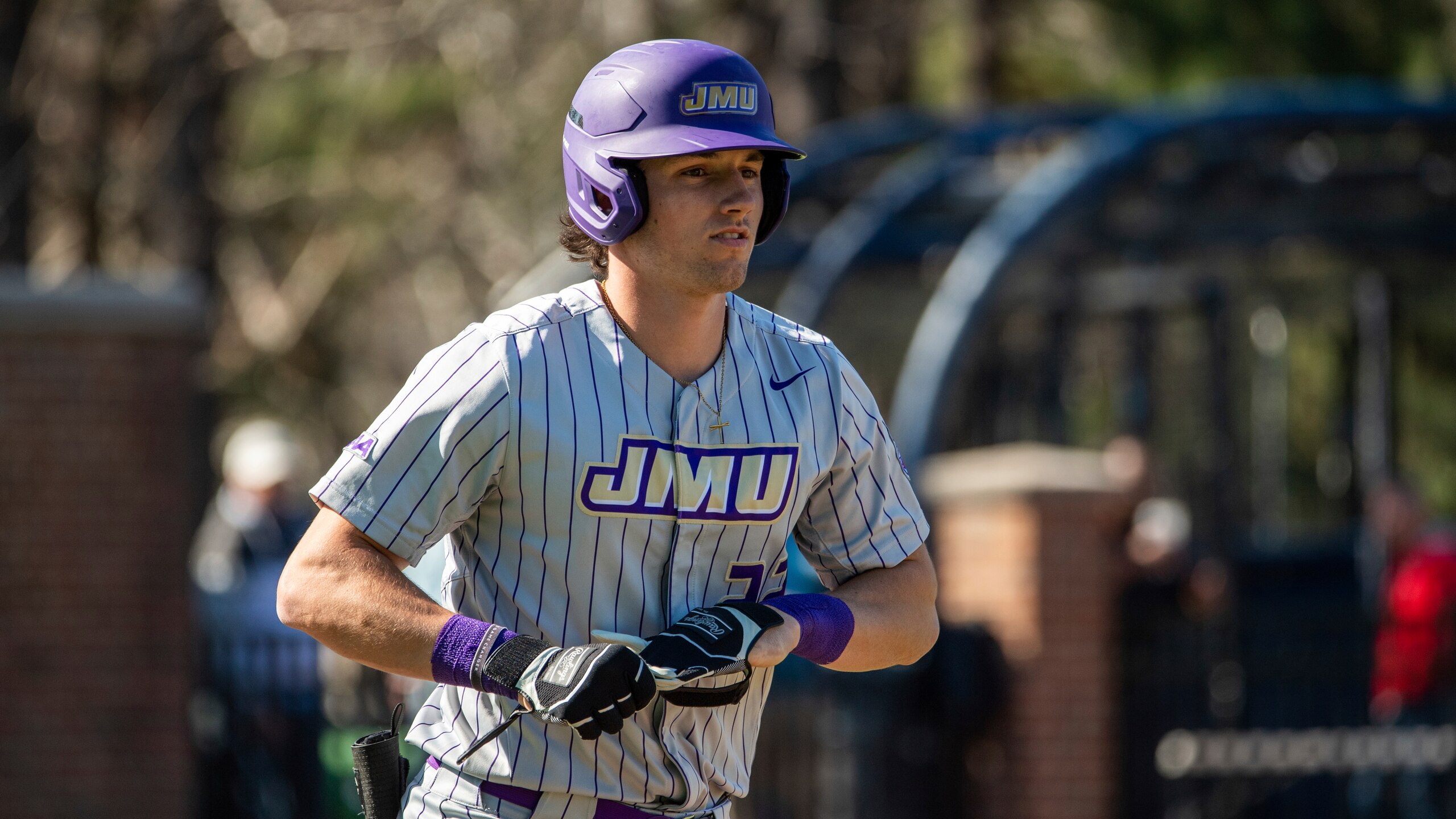 James Madison outfielder Chase DeLauter (22) takes off his gear as he heads to first base after being walked during an NCAA baseball game on Wednesday, April 2, 2022 in Richmond, Va. (AP Photo/Mike Caudill)