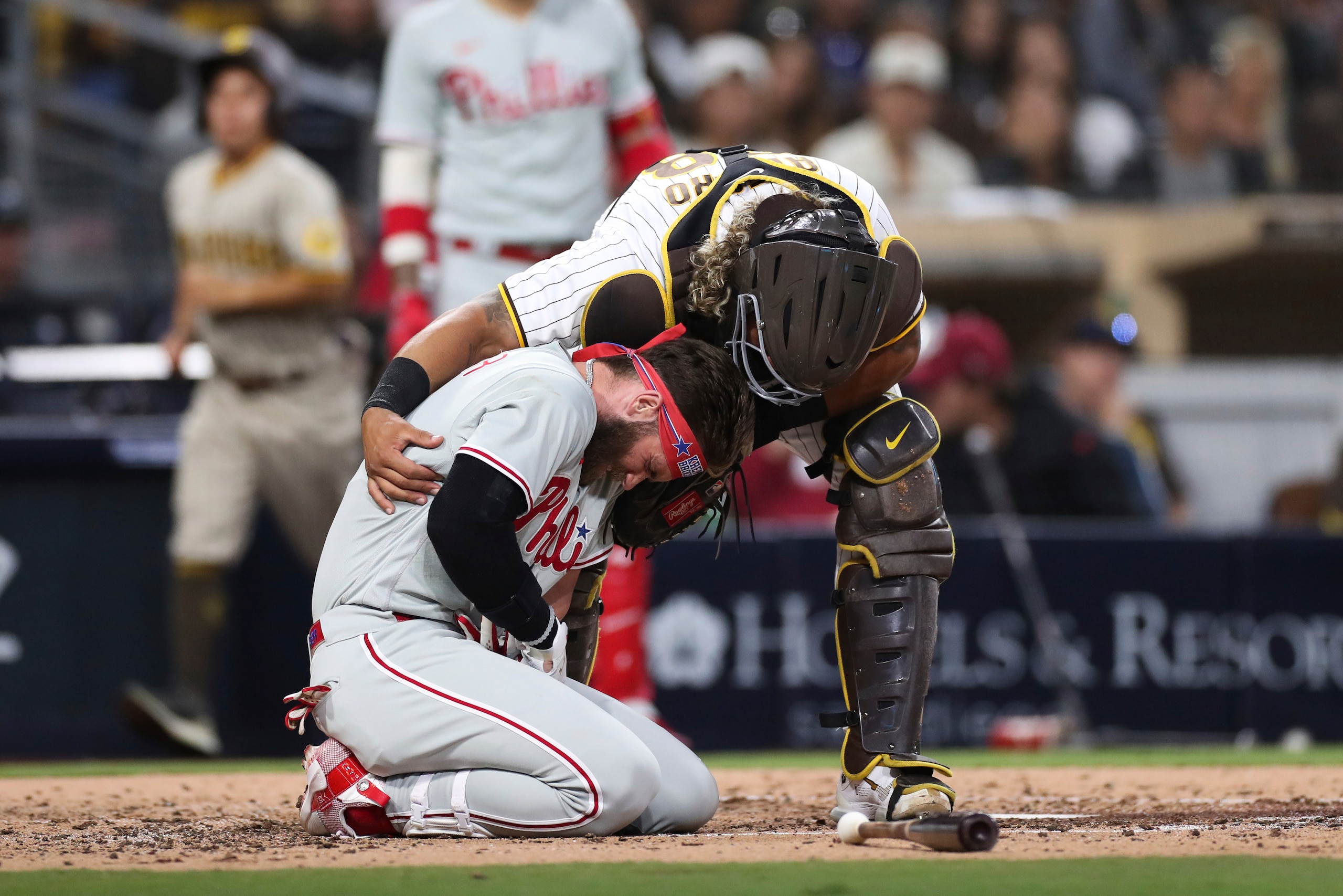 Bryce Harper, de rodillas, de los Filis de Filadelfia, reacciona después de haber sido golpeado por un lanzamiento de Blake Snell, lanzador de los Padres de San Diego, mientras el catcher Jorge Alfaro lo revisa durante la cuarta entrada del juego de béisbol, el sábado 25 de junio de 2022, en San Diego. (AP Foto/Derrick Tuskan)