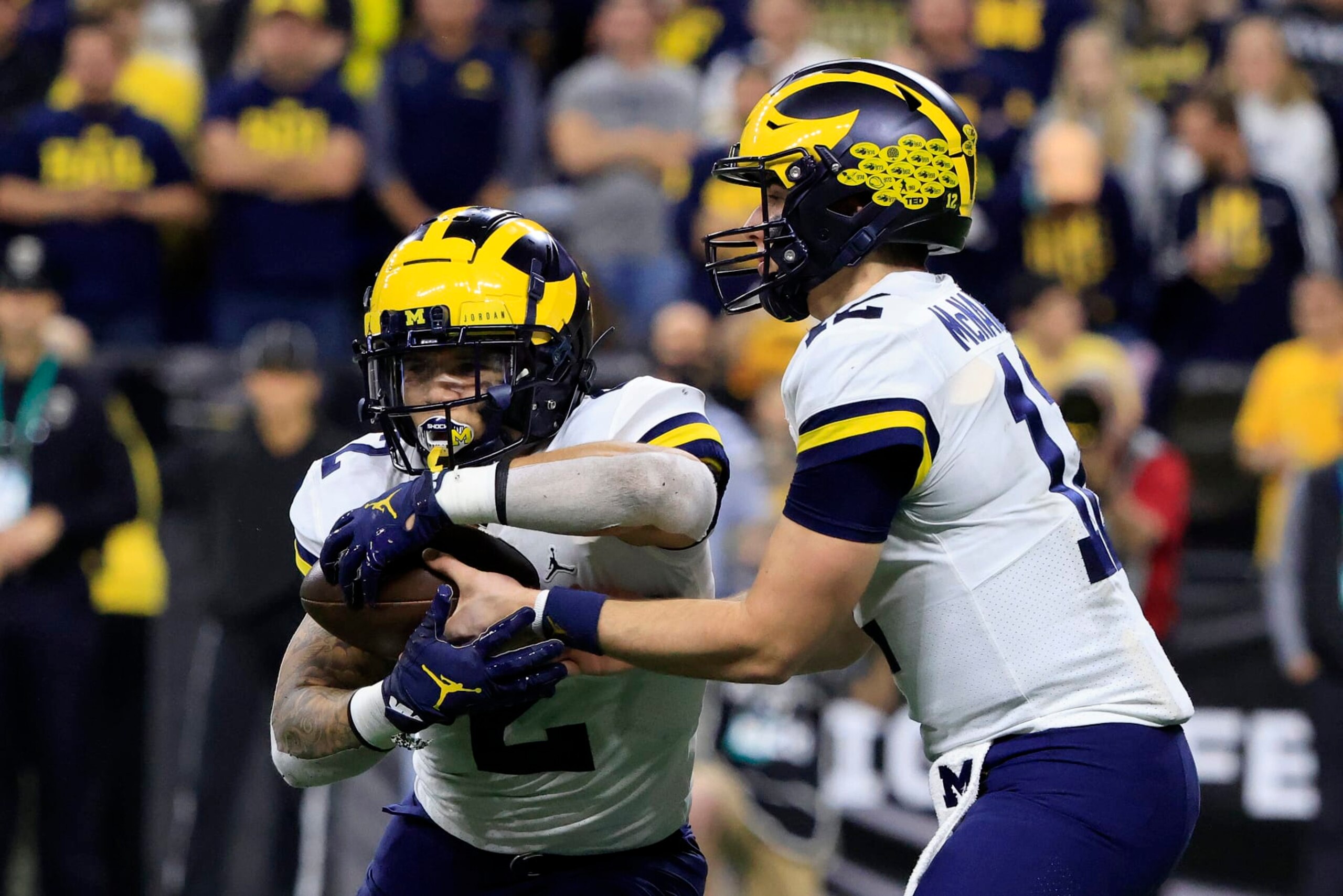 INDIANAPOLIS, INDIANA - DECEMBER 04: Cade McNamara #12 of the Michigan Wolverines hands the ball off to Blake Corum #2 of the Michigan Wolverines during the Big Ten Football Championship against the Iowa Hawkeyes at Lucas Oil Stadium on December 04, 2021 in Indianapolis, Indiana. (Photo by Justin Casterline/Getty Images)