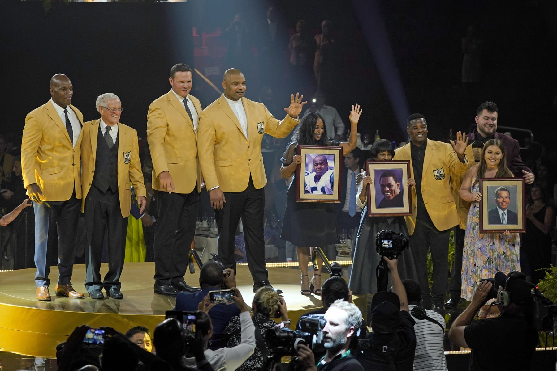 CORRECTS THAT ELAINE ANDERSON IS CLIFF BRANCH'S SISTER, NOT WIDOW - The members of the Pro Football Hall of Fame Class of 2022 line up on stage after receiving their gold jackets during the gold jacket dinner in Canton, Ohio, Friday, Aug. 5, 2022. From left to right, are: Bryant Young; Dick Vermeil; Tony Boselli; Richard Seymour; a photo of Sam Mills held by his widow, Melanie Mills; a photo of Cliff Branch held by his sister, Elaine Anderson; LeRoy Butler; and a photo of Art McNally held by his grandchildren Connor and Shannon McNally. (AP Photo/Gene J. Puskar)