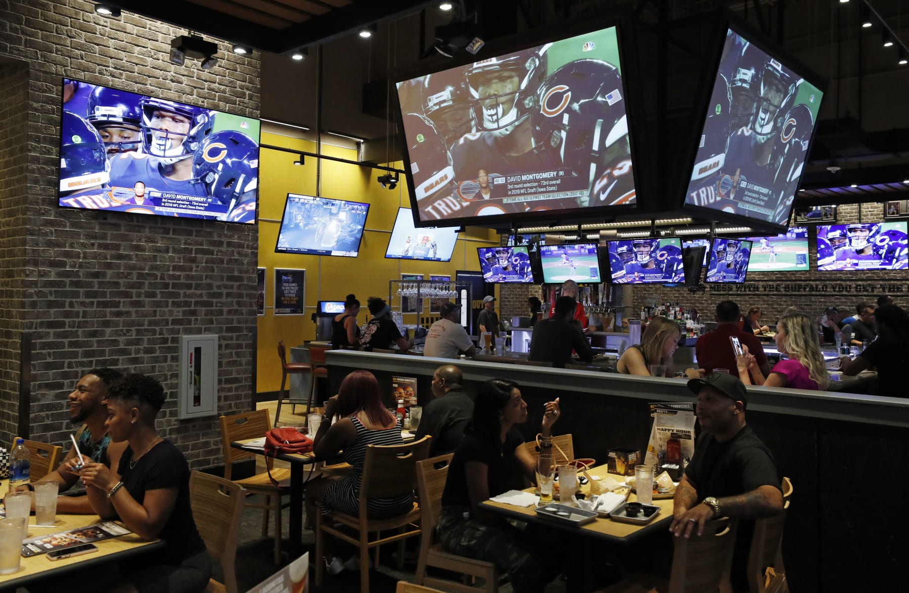 People eat and watch football at a Buffalo Wild Wings, Thursday, Sept. 5, 2019, in Las Vegas. MGM Resorts International and Buffalo Wild Wings are launching a mobile football game app for customers to pick favorite NFL teams, choose weekly fantasy performers and make proposition picks. Officials said the goal is to expand later at Buffalo Wild Wings in states where sports betting is legal through a mobile app called BetMGM. (AP Photo/John Locher)