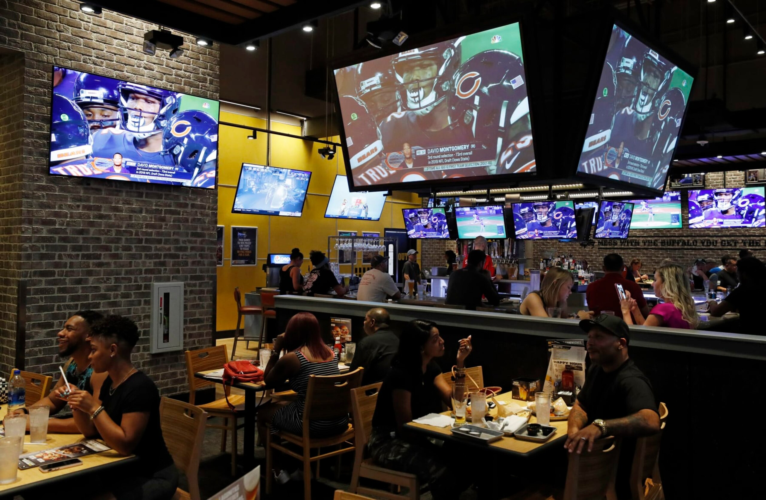 People eat and watch football at a Buffalo Wild Wings, Thursday, Sept. 5, 2019, in Las Vegas. MGM Resorts International and Buffalo Wild Wings are launching a mobile football game app for customers to pick favorite NFL teams, choose weekly fantasy performers and make proposition picks. Officials said the goal is to expand later at Buffalo Wild Wings in states where sports betting is legal through a mobile app called BetMGM. (AP Photo/John Locher)