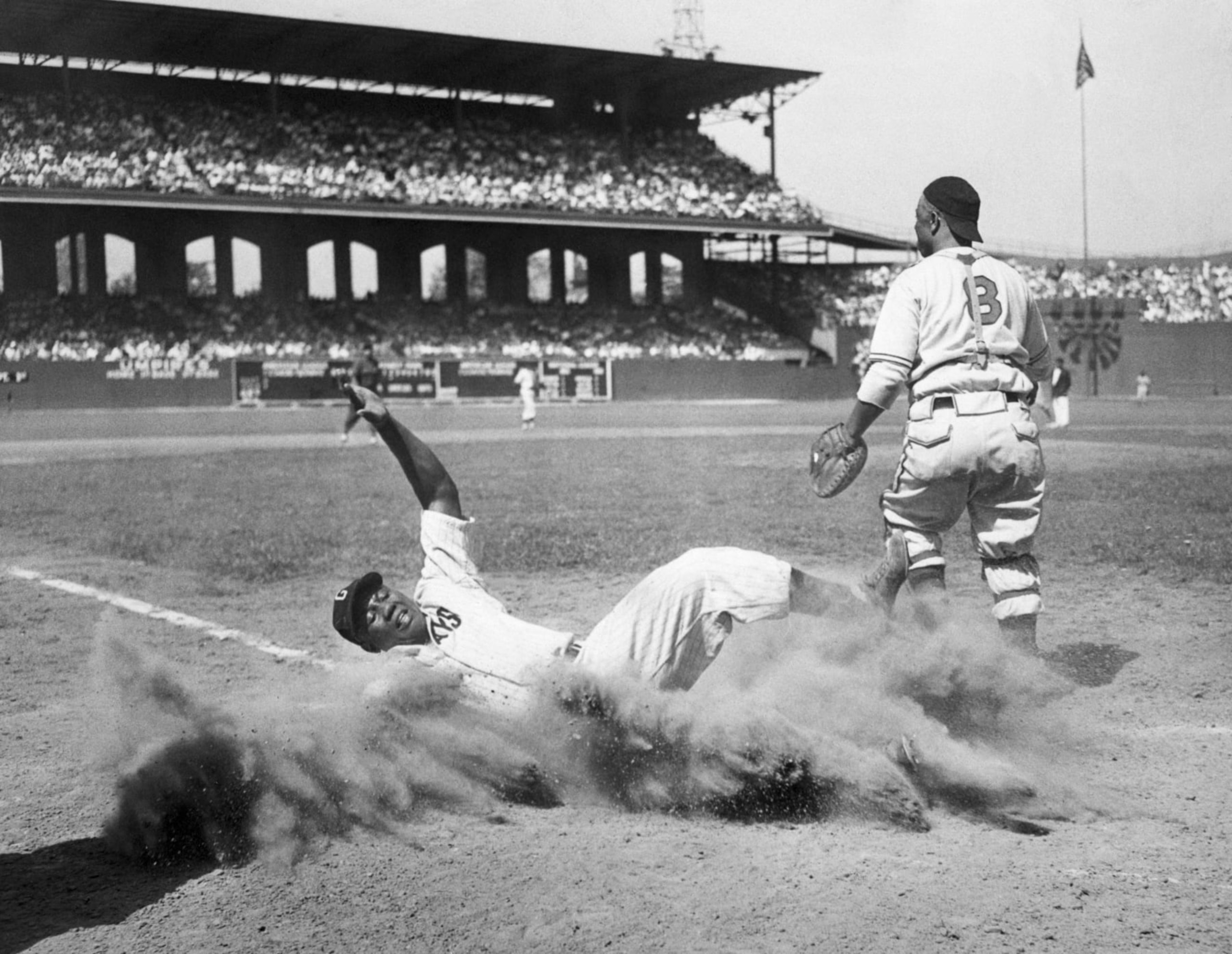 During the 12th annual East-West All-Star Game of the Negro Leagues, American baseball player Josh Gibson (1911 - 1947), of the East team, creates a cloud of dust as he slides into home plate during the fourth inning, Comiskey Park, Chicago, Illinois, August 13, 1944. West team’s catcher Ted Radcliffe (1902 - 2005) is visible at right. The West defeated the East, 7-4.