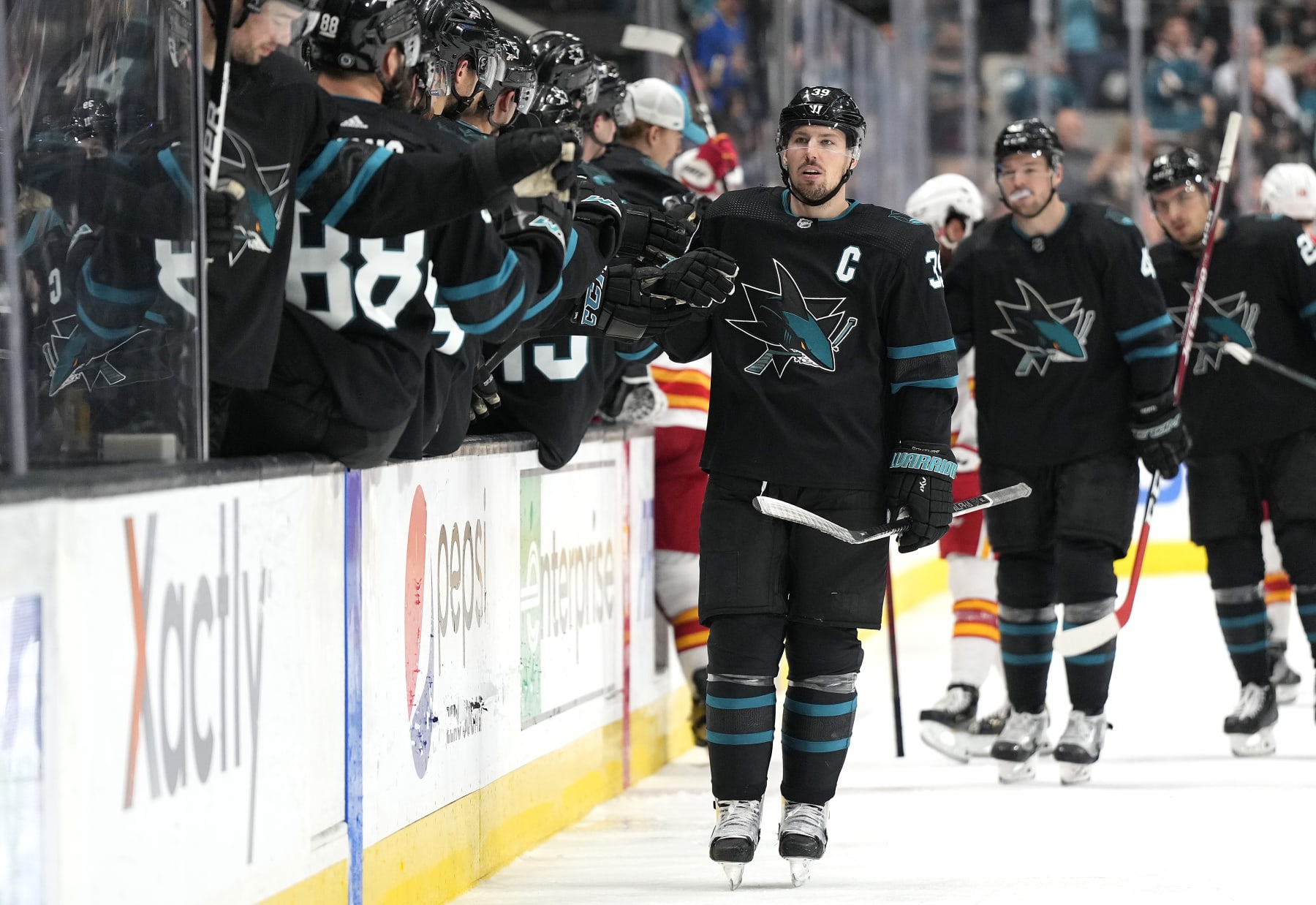 SAN JOSE, CALIFORNIA - APRIL 07: Logan Couture #39 of the San Jose Sharks is congratulated by teammates after he scored a goal against the Calgary Flames during the third period of an NHL hockey game at SAP Center on April 07, 2022 in San Jose, California. (Photo by Thearon W. Henderson/Getty Images)