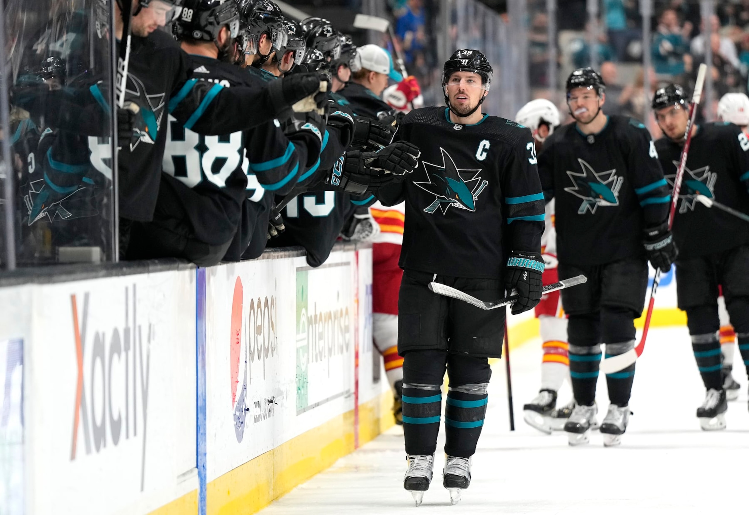 SAN JOSE, CALIFORNIA - APRIL 07: Logan Couture #39 of the San Jose Sharks is congratulated by teammates after he scored a goal against the Calgary Flames during the third period of an NHL hockey game at SAP Center on April 07, 2022 in San Jose, California. (Photo by Thearon W. Henderson/Getty Images)