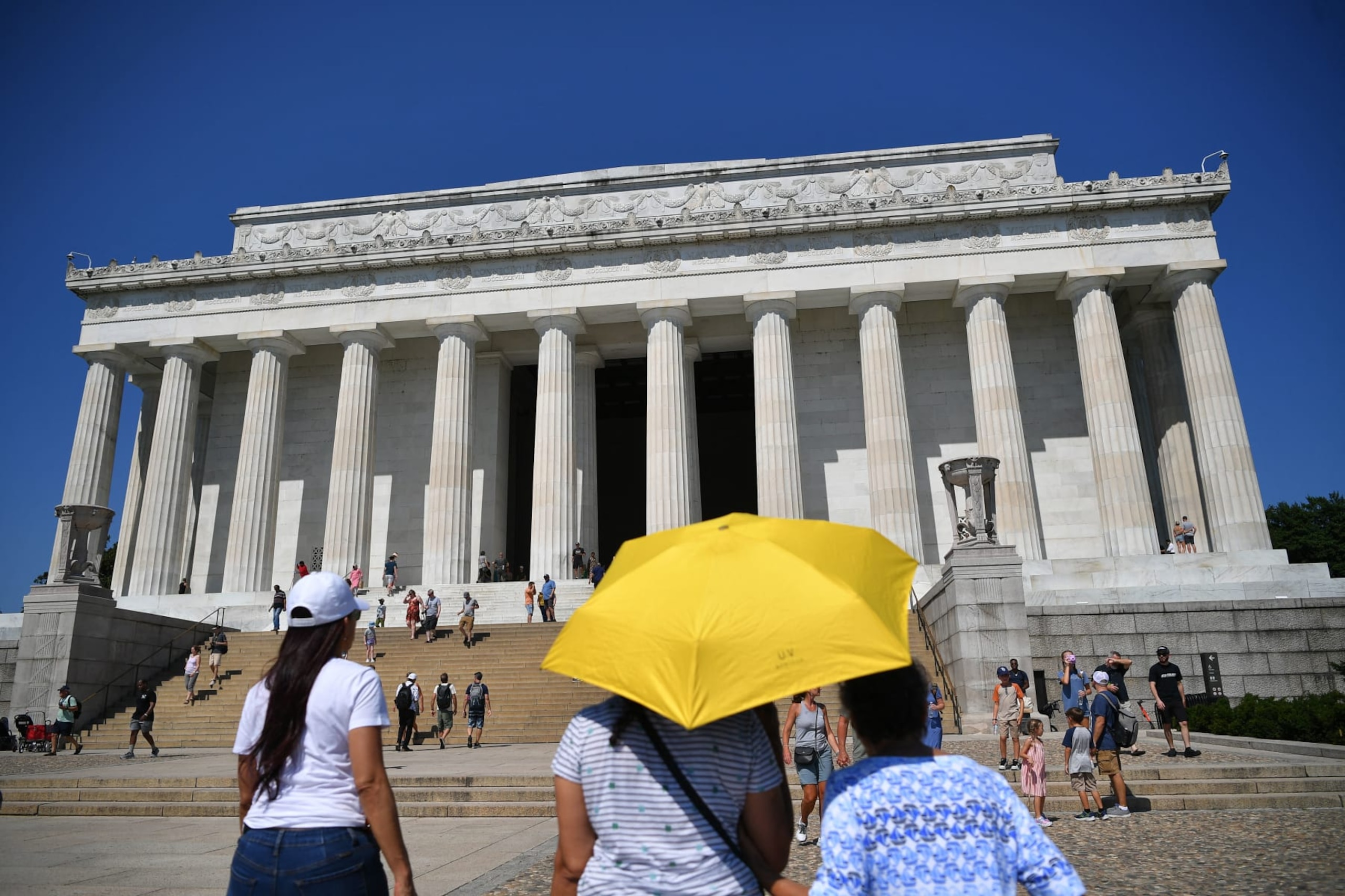 TOPSHOT - Visitors to the Lincoln Memorial use an umbrella to shelter from the Sun in Washington, DC, on July 23, 2022. - The heat wave blanketing the region is expect to peak this weekend with temperatures near 38C (100F.) (Photo by MANDEL NGAN / AFP) (Photo by MANDEL NGAN/AFP via Getty Images)