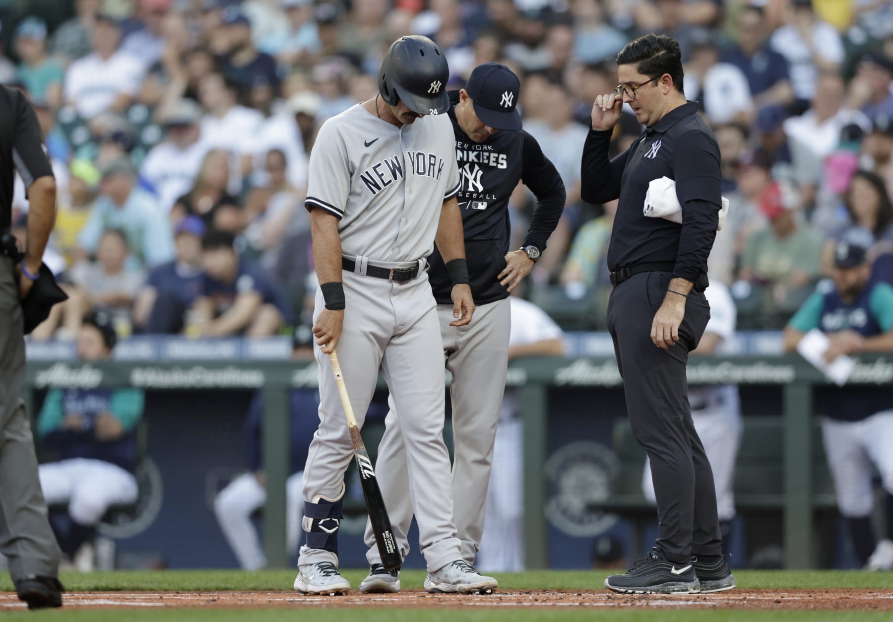 New York Yankees manager Aaron Boone, back and a trainer, right, talk with Matt Carpenter after he fouled a ball off his ankle against the Seattle Mariners during the first inning of a baseball game, Monday, Aug. 8, 2022, in Seattle. He was replaced in the lineup after his at bat. (AP Photo/John Froschauer)