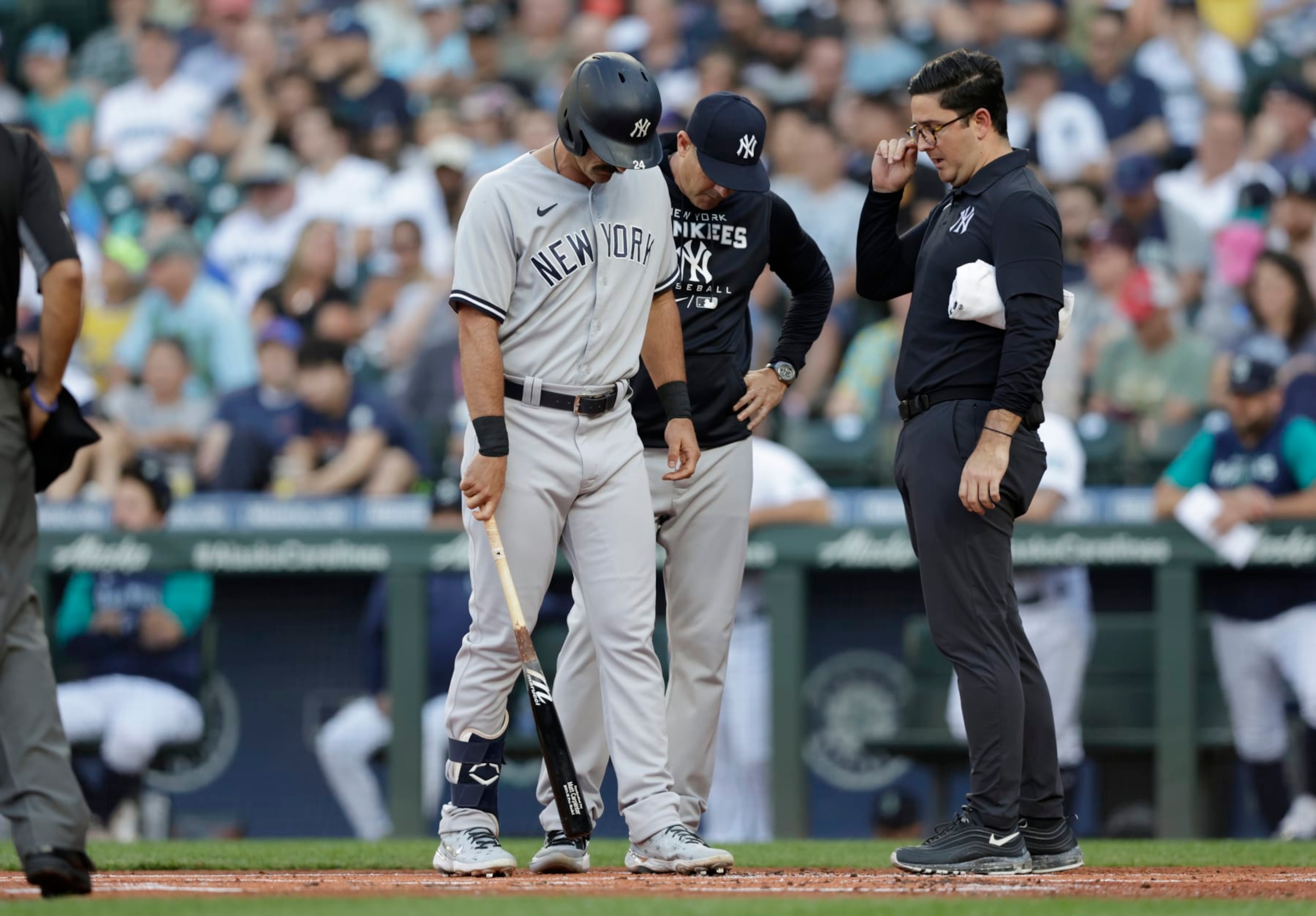 New York Yankees manager Aaron Boone, back and a trainer, right, talk with Matt Carpenter after he fouled a ball off his ankle against the Seattle Mariners during the first inning of a baseball game, Monday, Aug. 8, 2022, in Seattle. He was replaced in the lineup after his at bat. (AP Photo/John Froschauer)